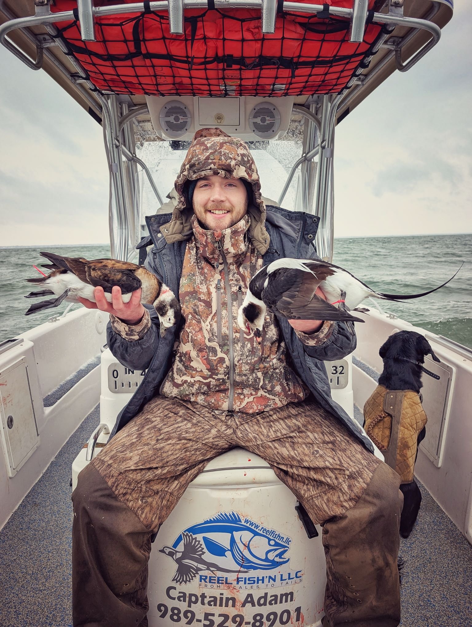 A happy waterfowler holding a brace of sea ducks shot from a layout boat during a late-season hunt on the open water of the Great Lakes.   
