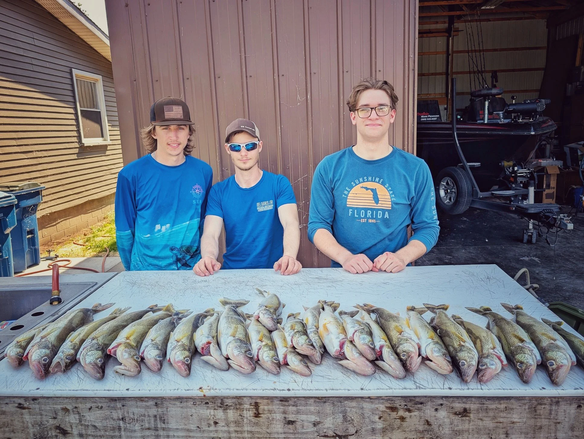  Three young men posing with a heavy spread of Saginaw Bay walleye on a cleaning table after a high-action Reel Fish'n fishing charter. 