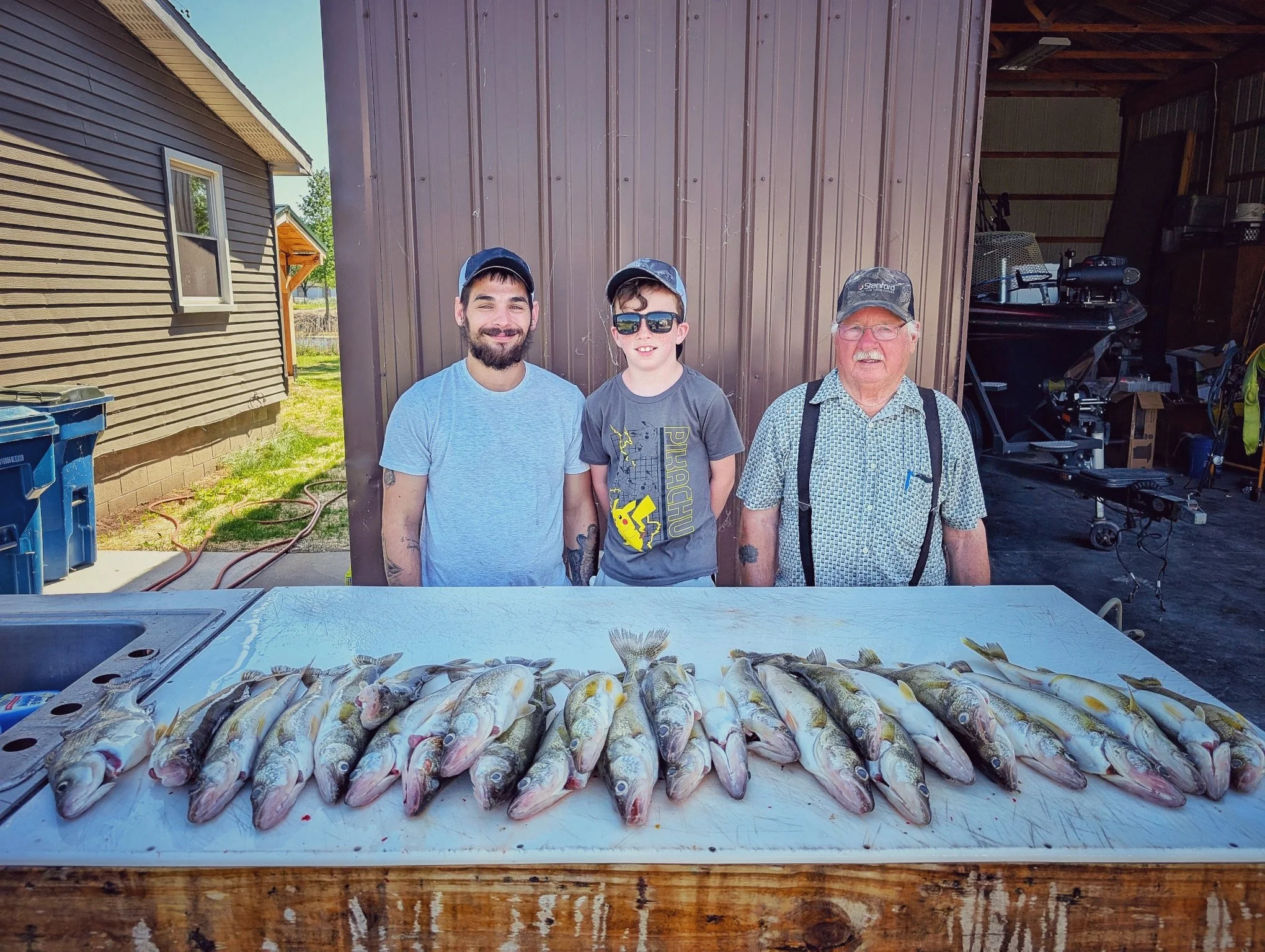  Three generations of anglers standing behind a full limit of Saginaw Bay walleye at the cleaning station after a successful Linwood, MI fishing charter. 