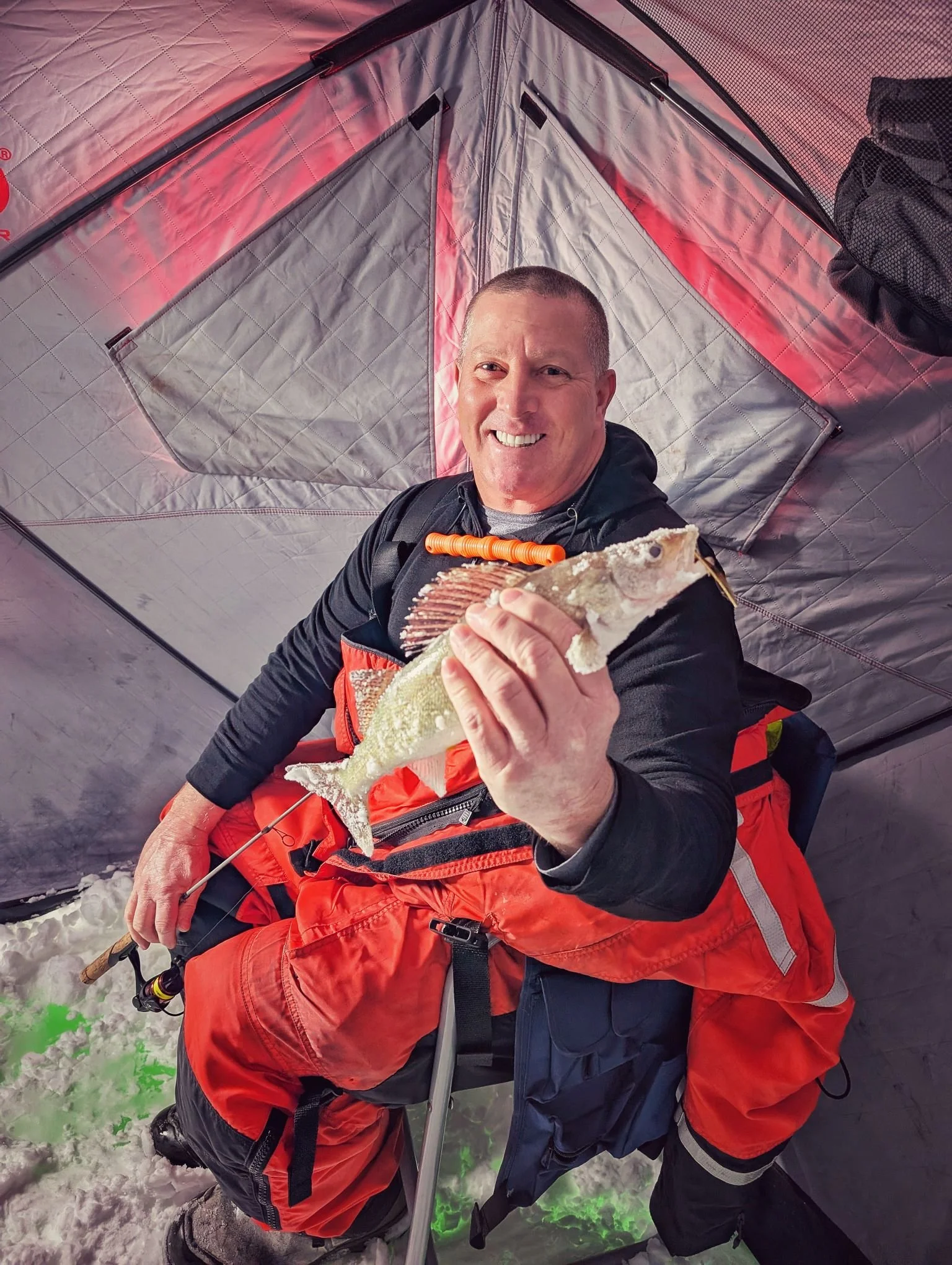  A happy client enjoying a comfortable day of ice fishing on Saginaw Bay, holding a fresh walleye inside a heated hub-style shanty.   