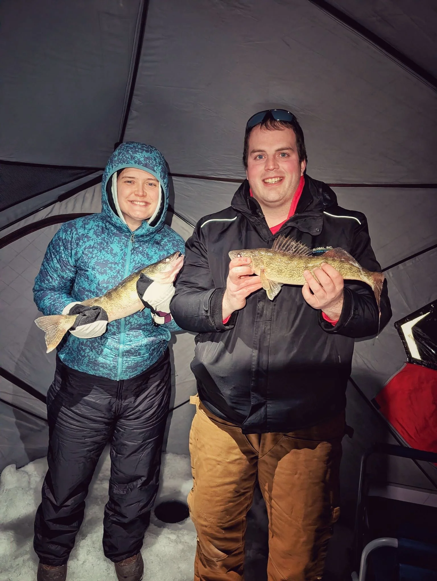  A happy couple holding their walleye catch inside a heated ice shanty during a successful Saginaw Bay winter fishing trip with Reel Fish'n.   