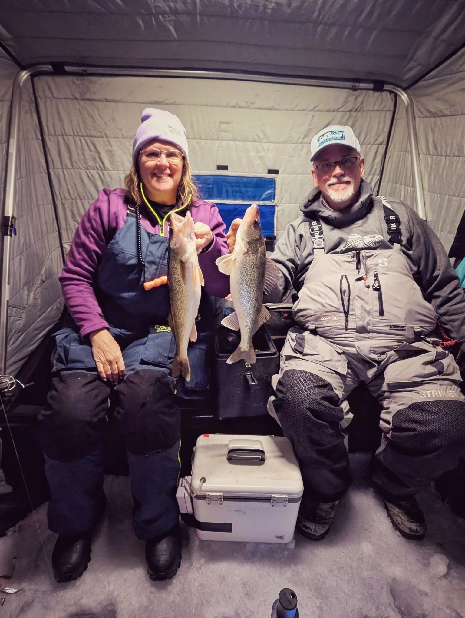  Happy clients displaying their walleye catch while sitting comfortably in a heated hub-style shanty during a Saginaw Bay ice fishing charter.   