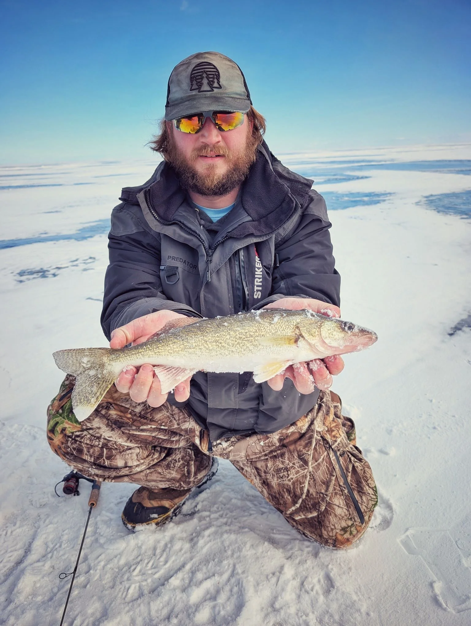  A successful angler kneeling on the frozen expanse of Saginaw Bay with a fresh walleye during a mobile ice fishing charter with Reel Fish'n.   