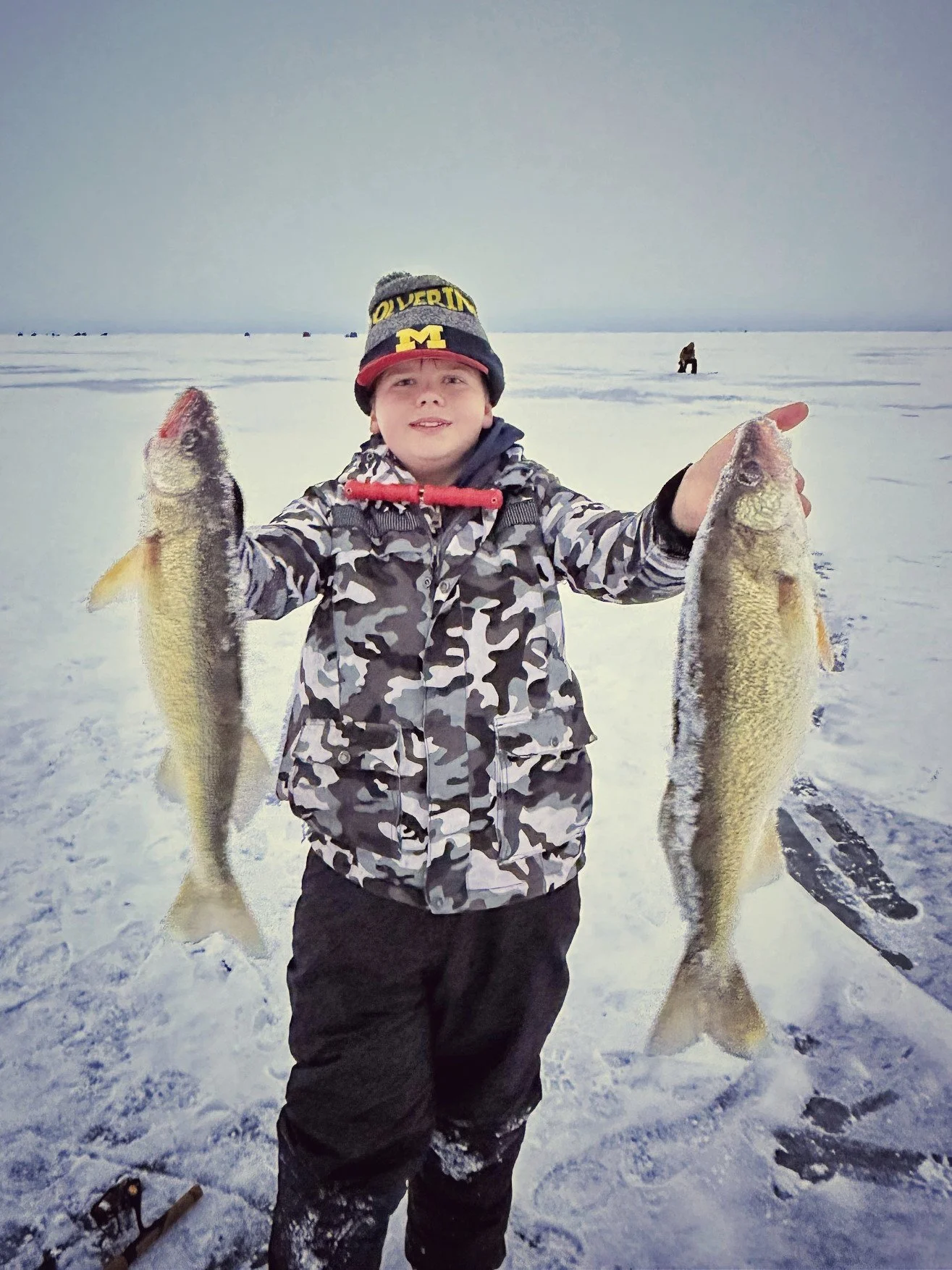  A young angler holding up two nice walleye caught during a family-friendly ice fishing charter on Saginaw Bay with Reel Fish'n.   