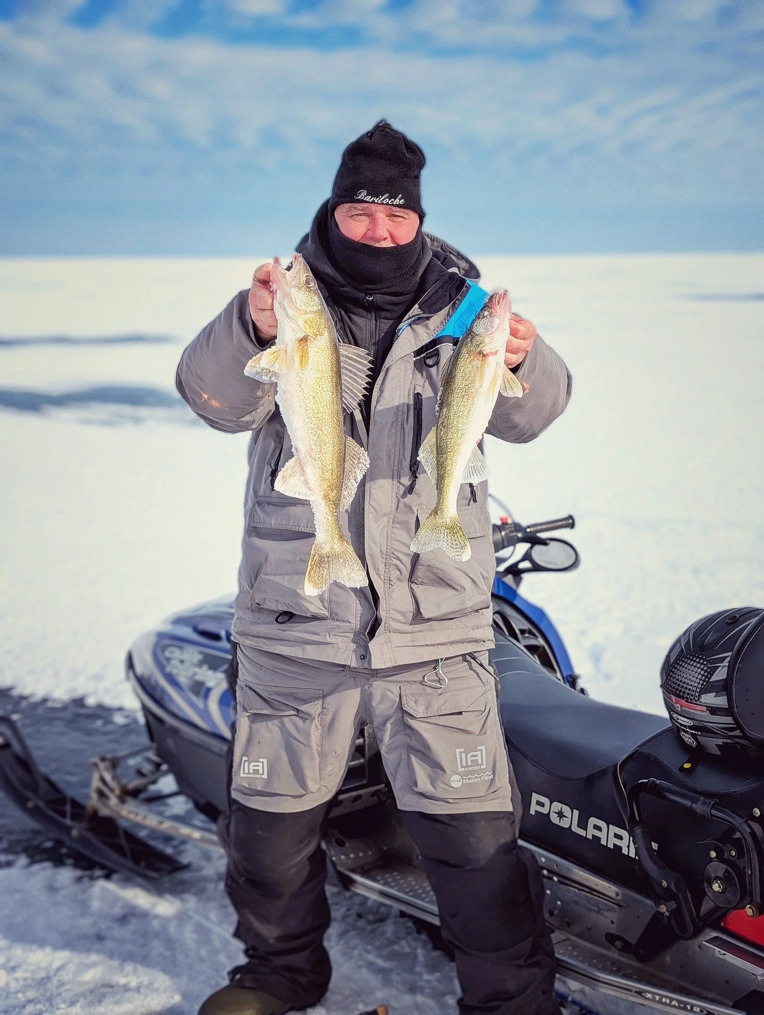  A successful angler with a brace of walleye standing next to a snowmobile on the frozen expanse of Saginaw Bay during a mobile ice fishing charter with Reel Fish'n.   