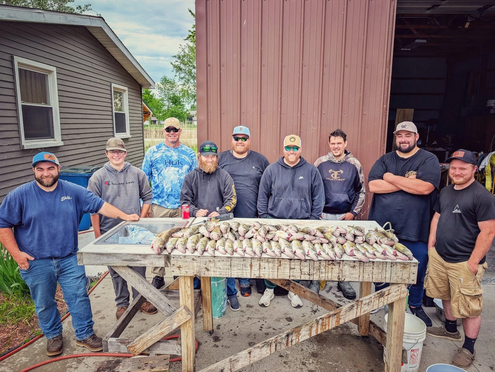  A large group of anglers posing with a massive limit of walleye at a cleaning station after a successful Saginaw Bay summer trolling charter.   
