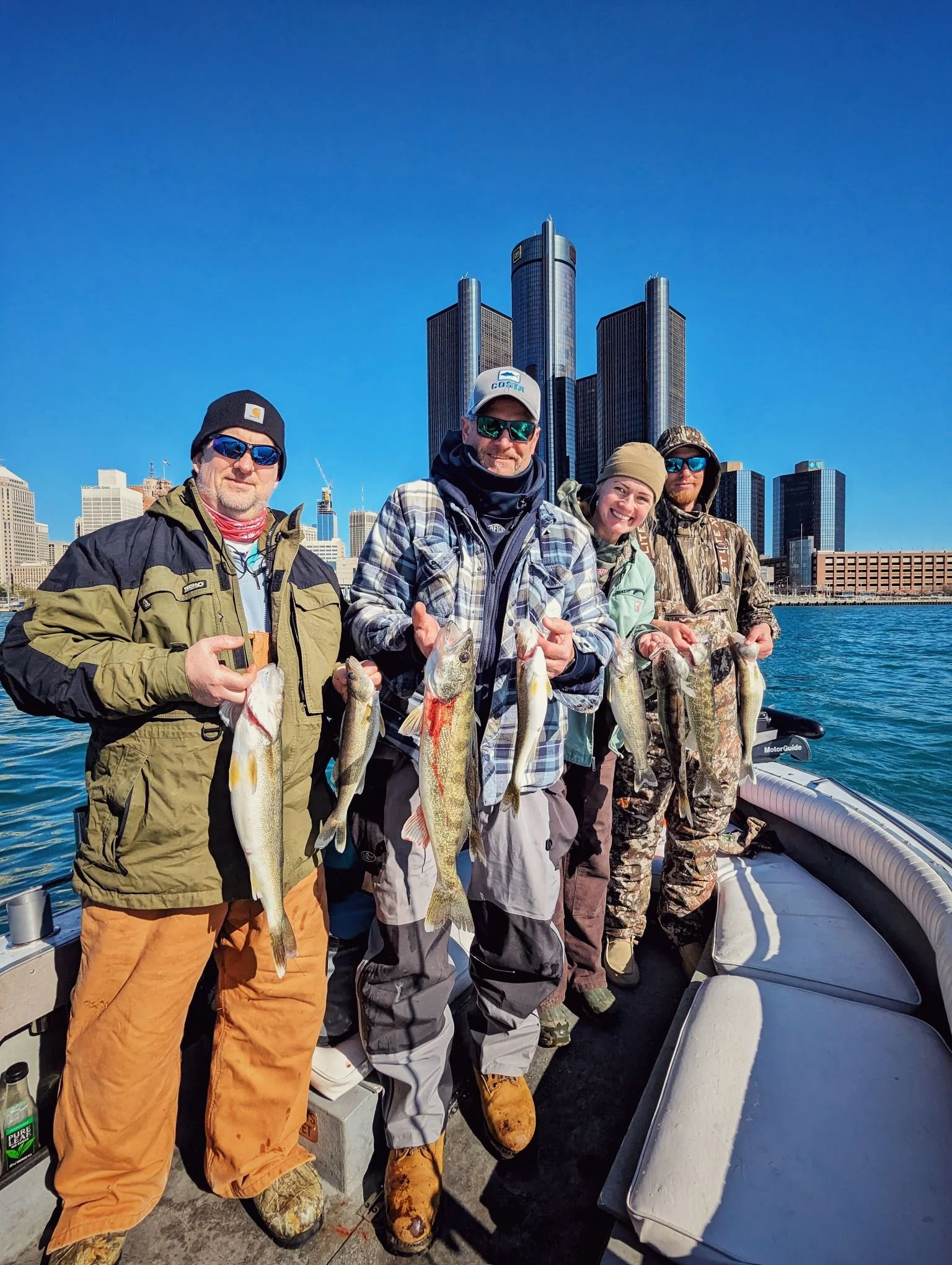  A group of happy clients holding up walleye on the boat with the Detroit Renaissance Center and city skyline in the background. 