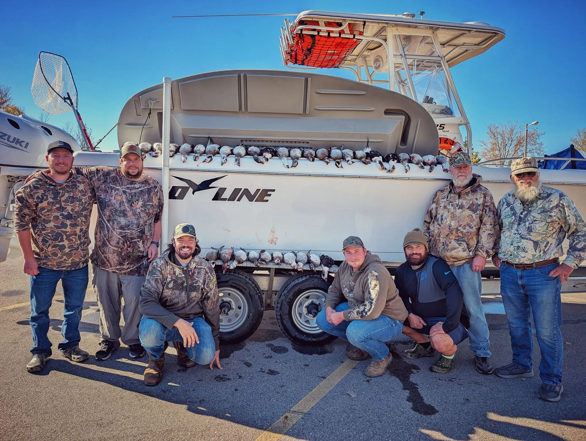  A large group of waterfowl hunters posing with a full limit of ducks displayed on the side of the 25ft Proline tender boat after a successful Great Lakes hunt.   