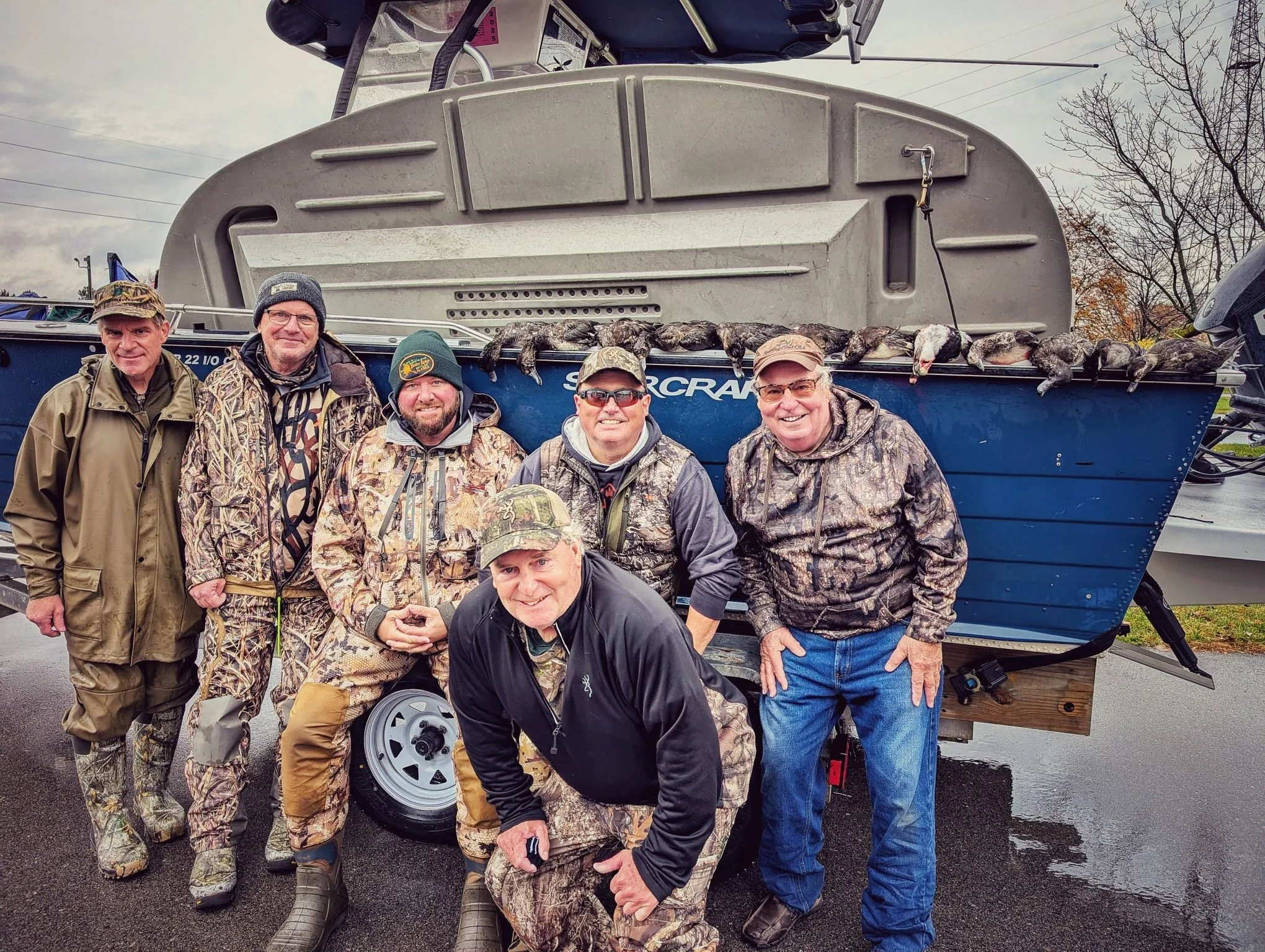  A group of six duck hunters posing in front of a specialized tender boat following a high-action morning of diver duck hunting. 
