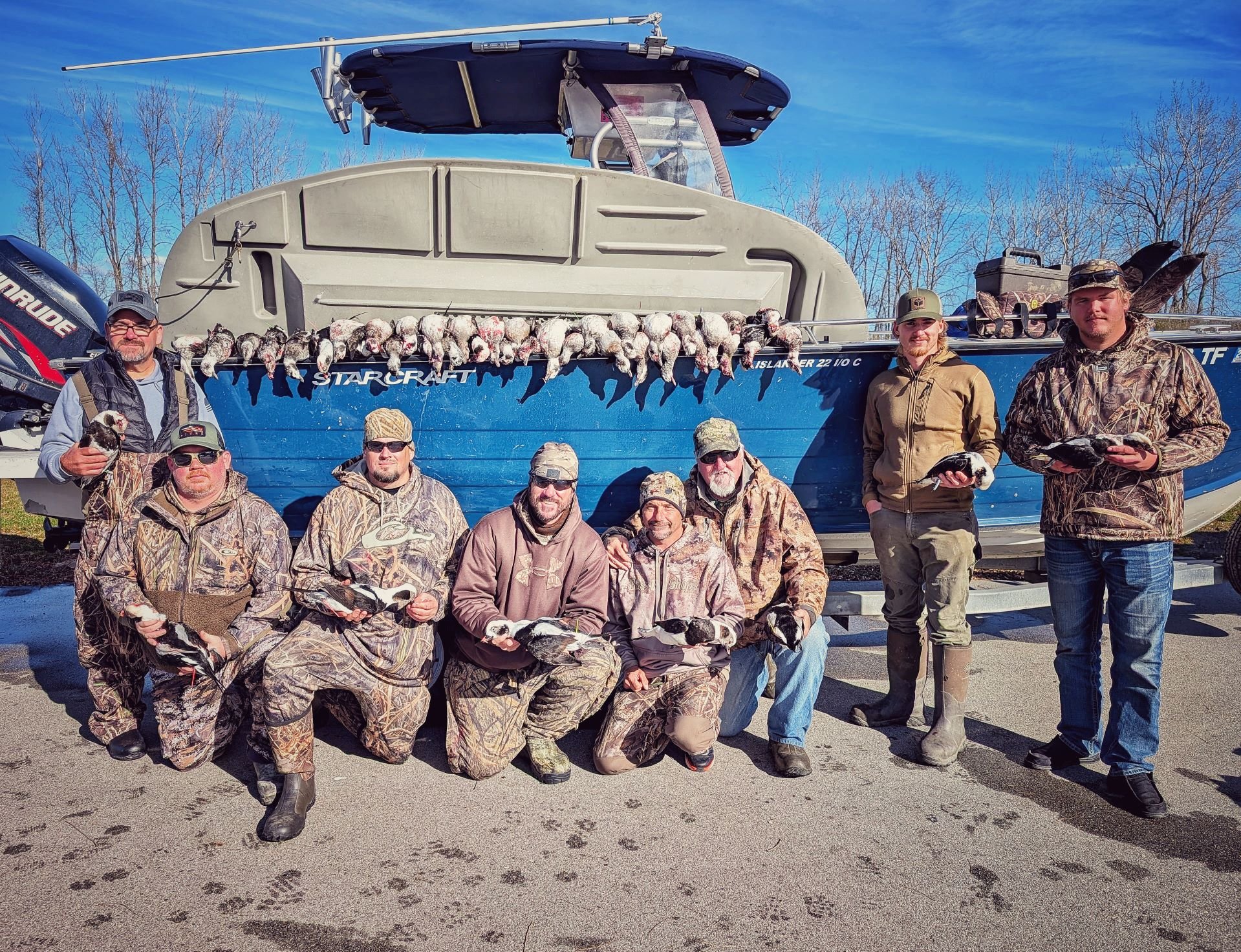  A large group of duck hunters posing with their morning harvest displayed on a blue tender boat after a successful open-water layout hunt with Reel Fish'n LLC. 