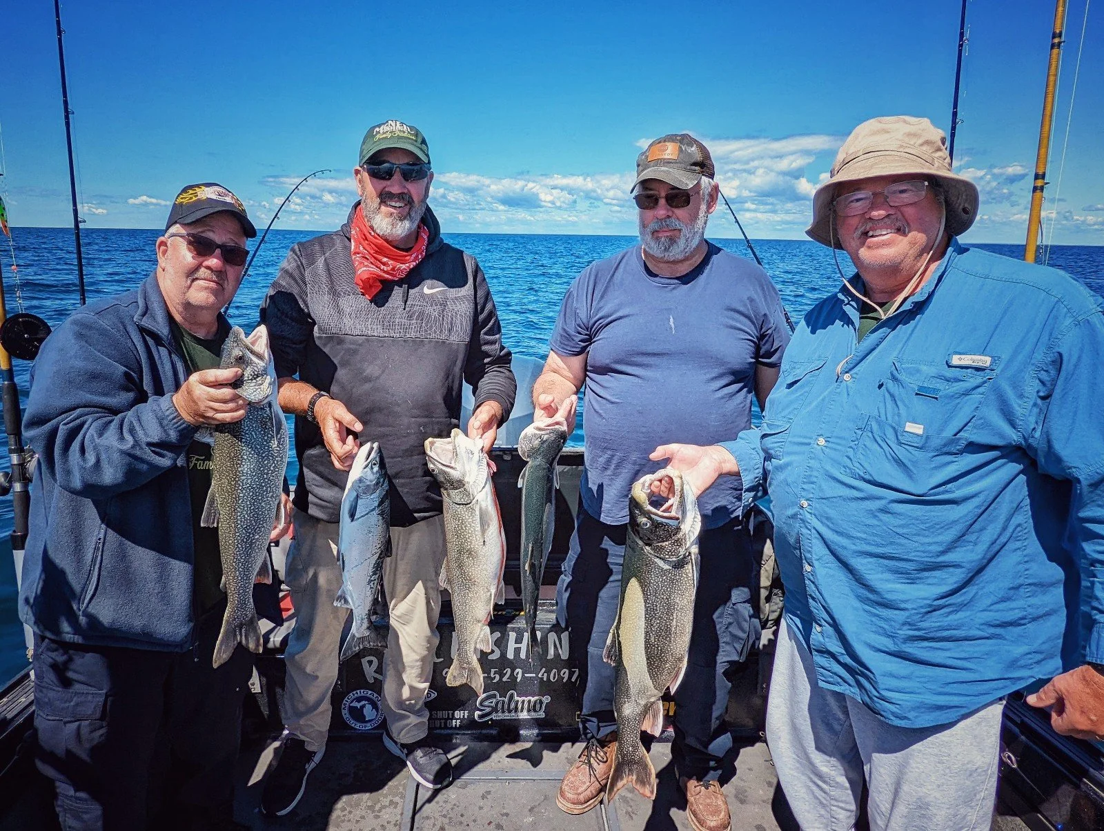 Four anglers on the deck of a boat proudly holding up a variety of fish including walleye and trout, highlighting the hands-on coaching provided by Reel Fish’n captains.
