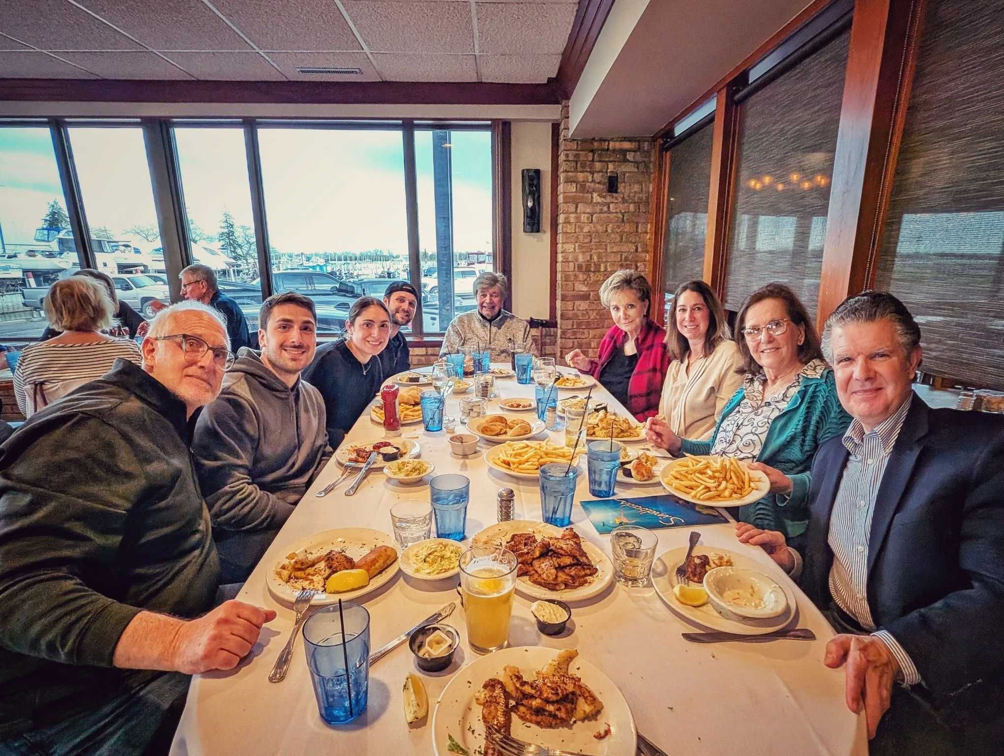 A large group of corporate clients smiling and enjoying a fresh walleye dinner at a waterfront restaurant following their multi-boat fishing charter.
