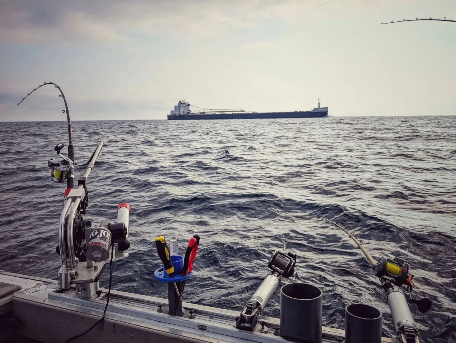 A trolling rod doubled over on Lake Huron out of Oscoda, MI, with a Great Lakes freighter passing in the distance during a Reel Fish'n trout and salmon charter.