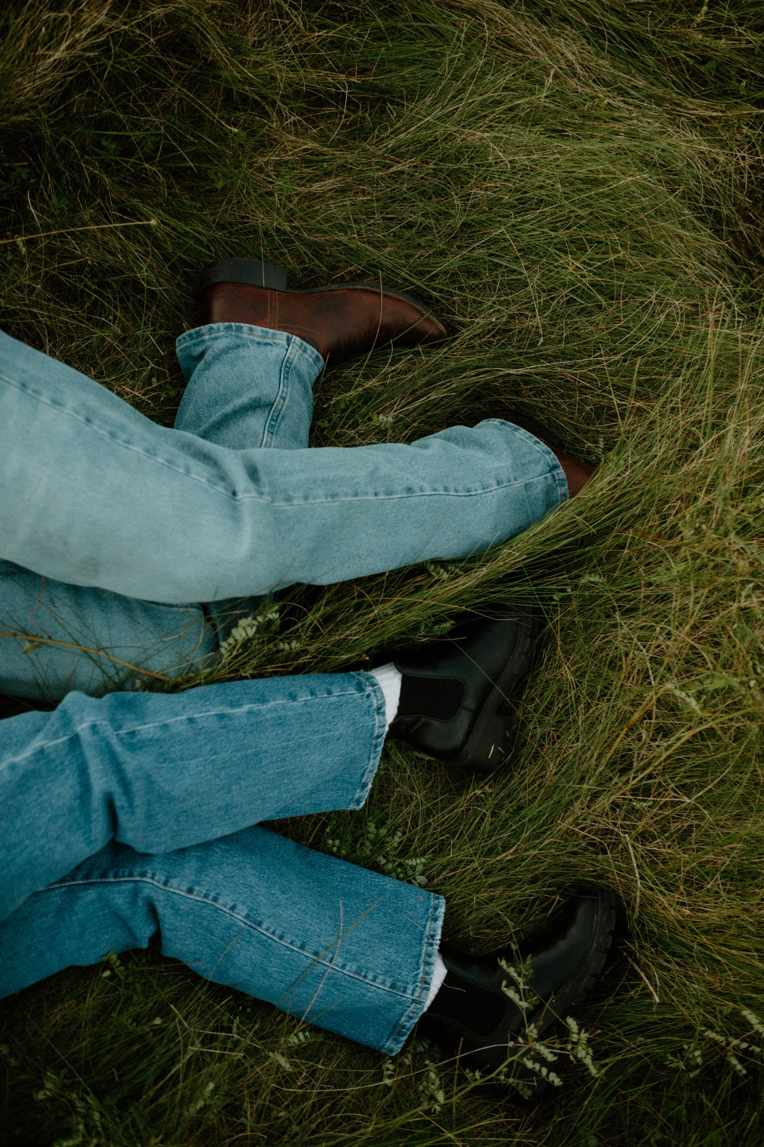 People wearing blue jeans and black shoes lying on grassy ground.