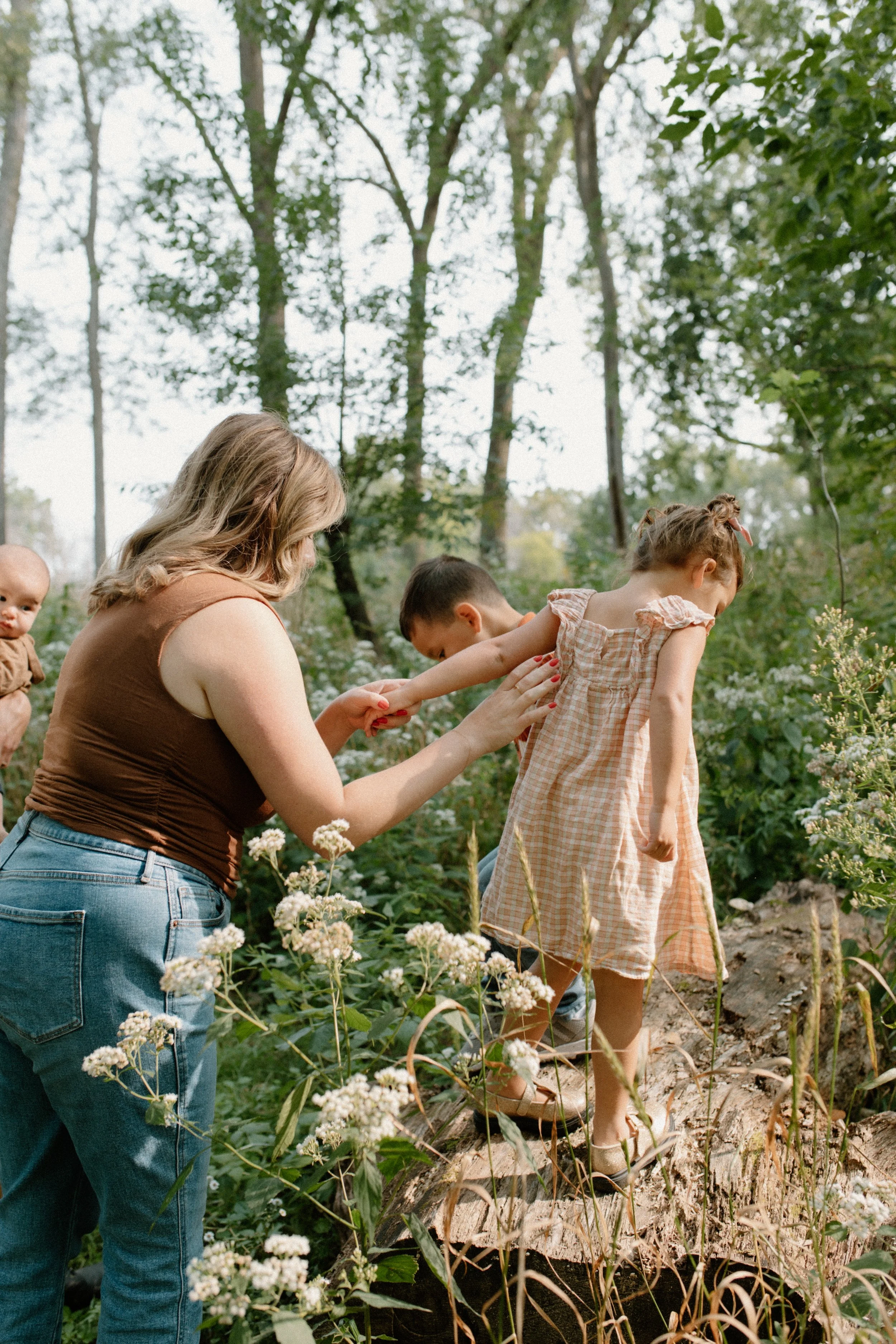 A woman and two children picking flowers in a garden or natural outdoor setting.