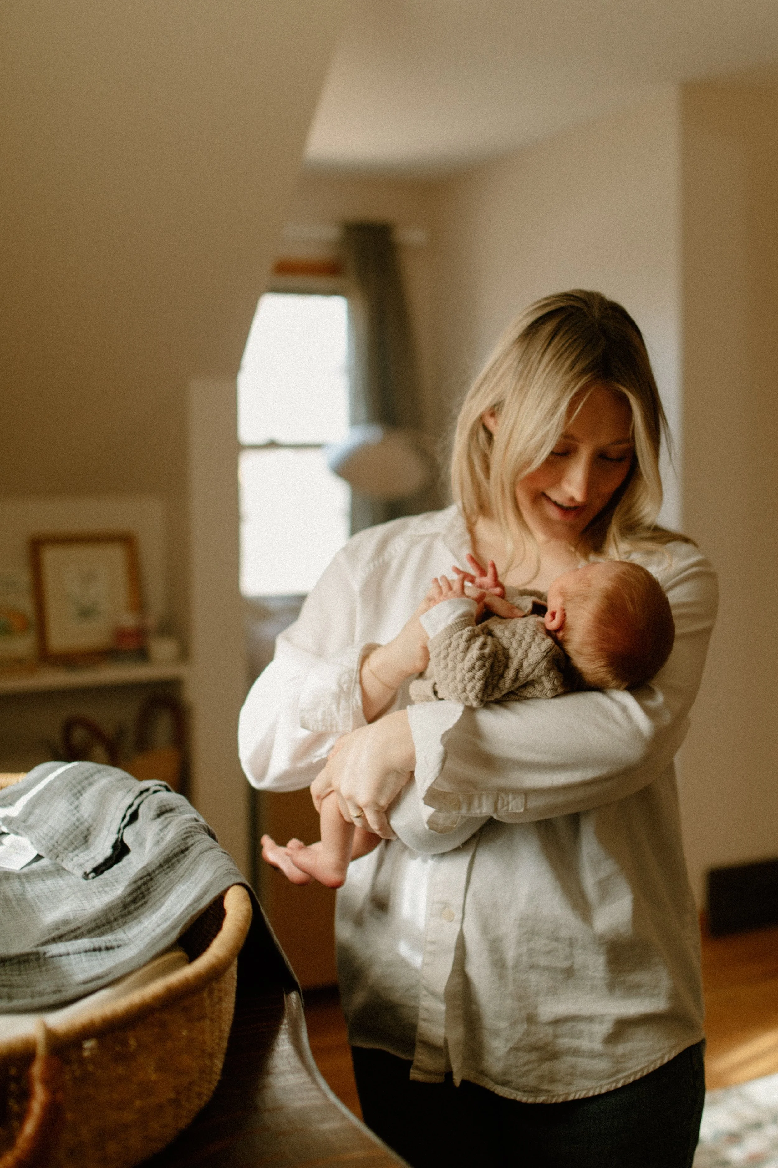 A woman lovingly holds a newborn baby in a cozy, softly lit room, smiling gently as she looks down at the infant.