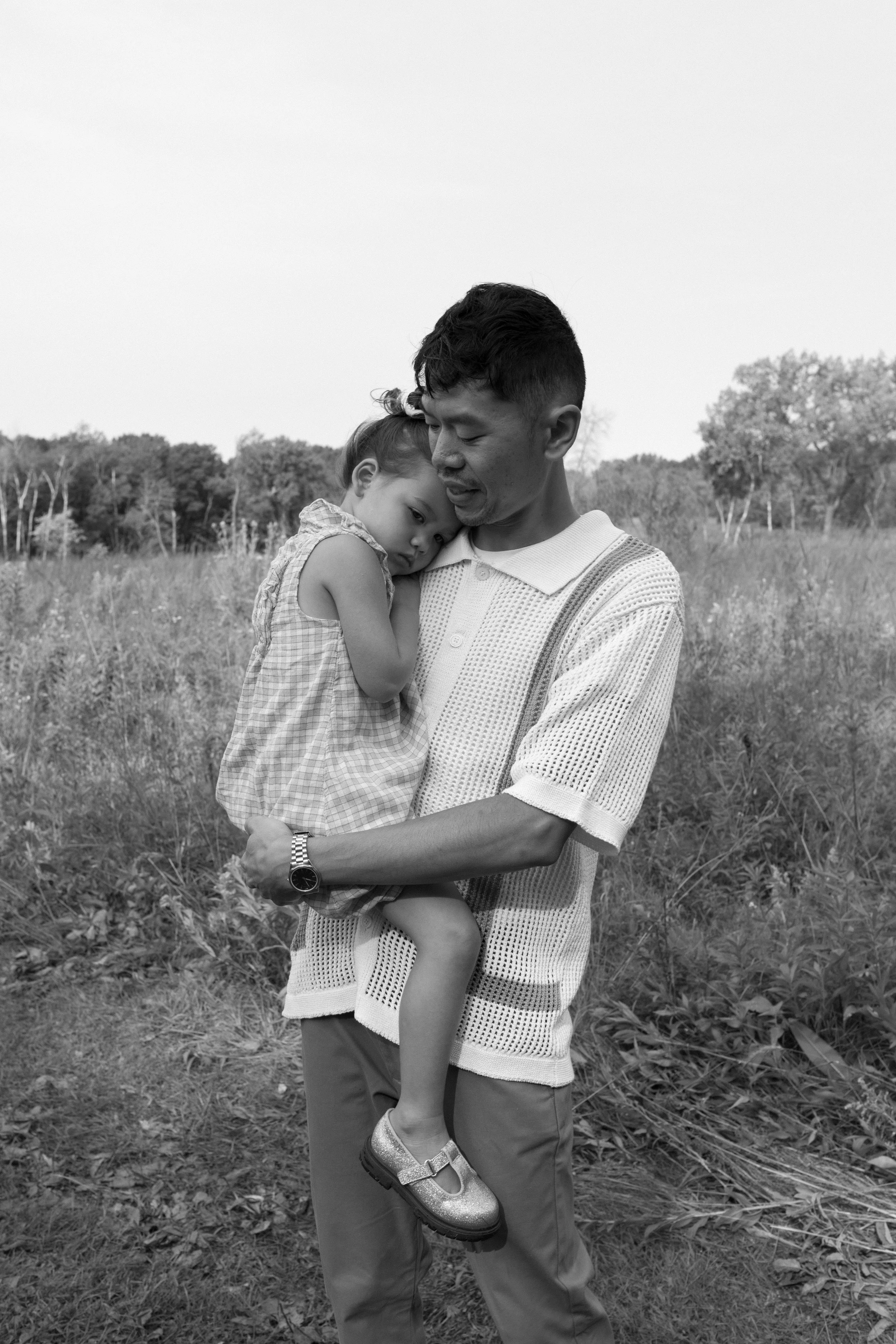 A man carrying a young girl in a field with trees in the background.