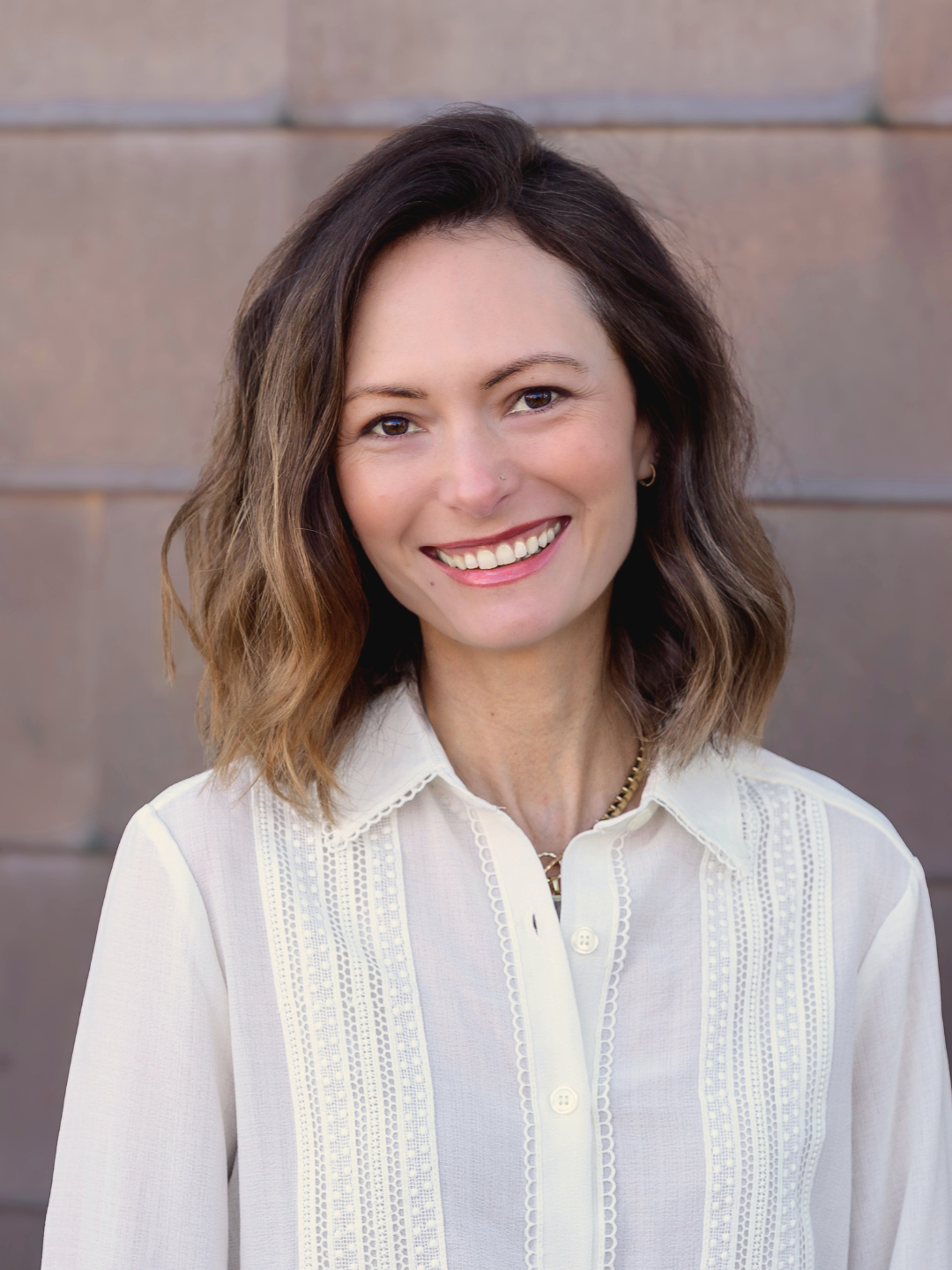 Woman with curly hair wearing a green shirt standing against a dark gray wall.