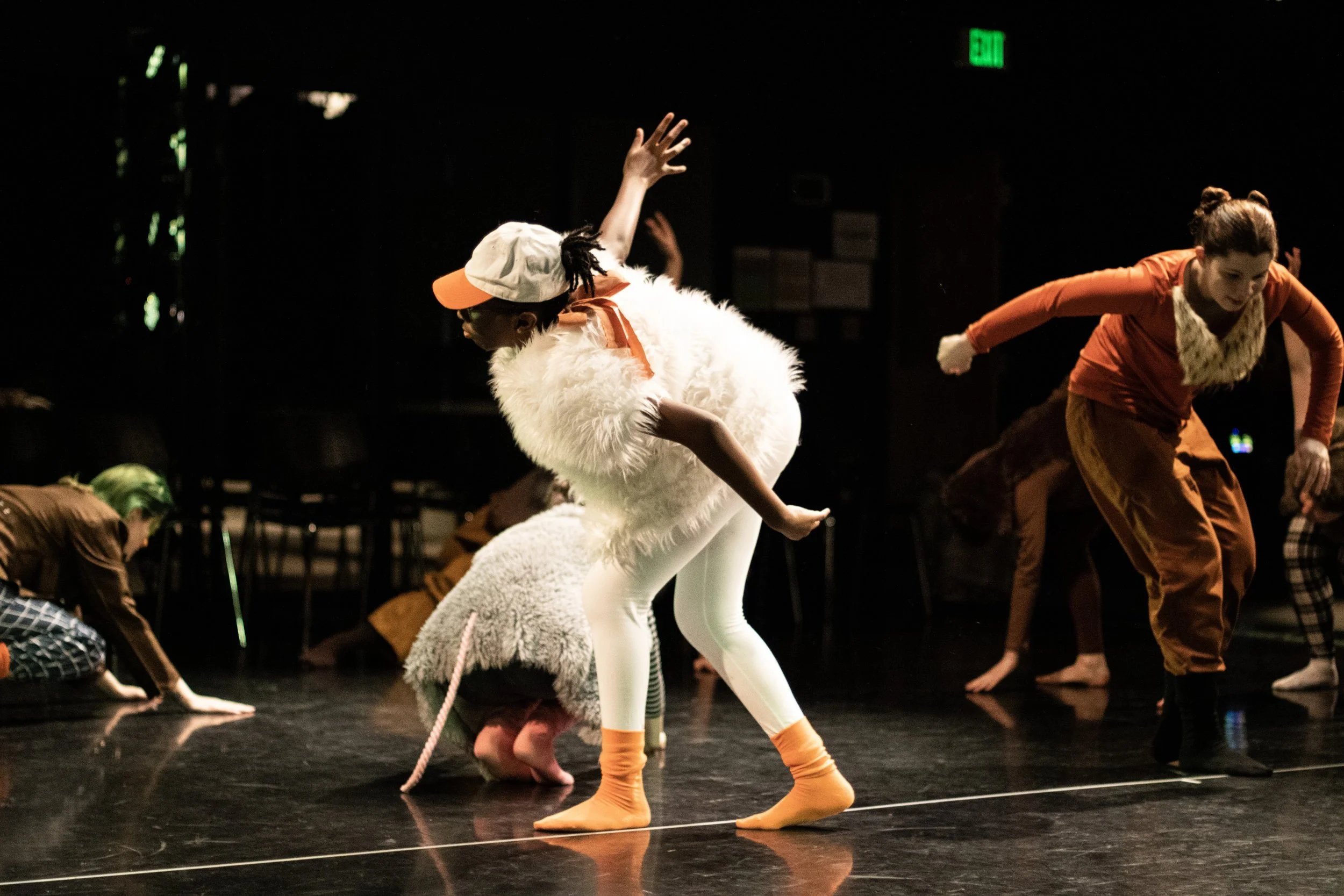 Children in colorful costumes performing on stage during a dance or theatrical rehearsal.