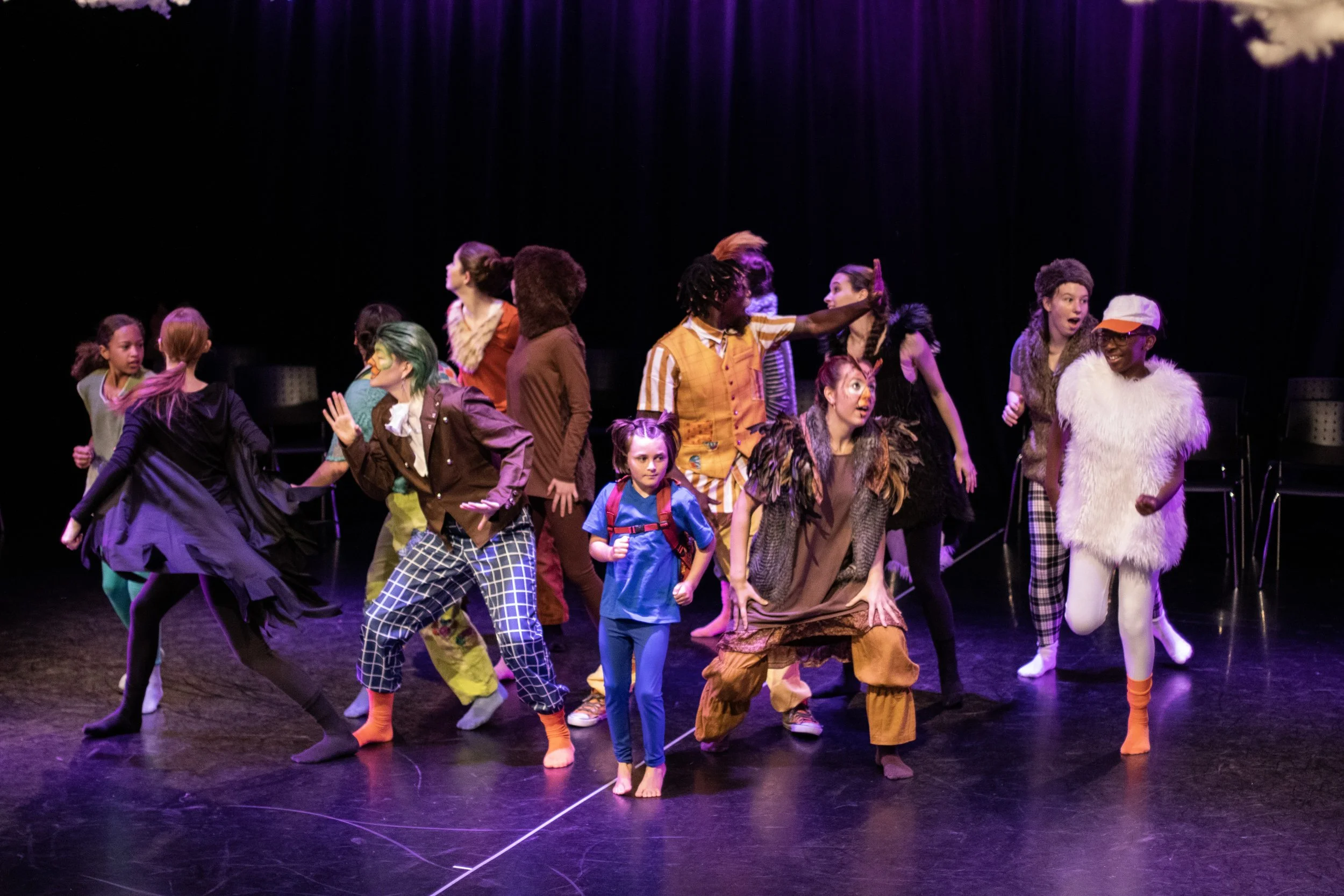 A diverse group of children performing on a stage, dressed in colorful costumes for a theatrical play or musical production.