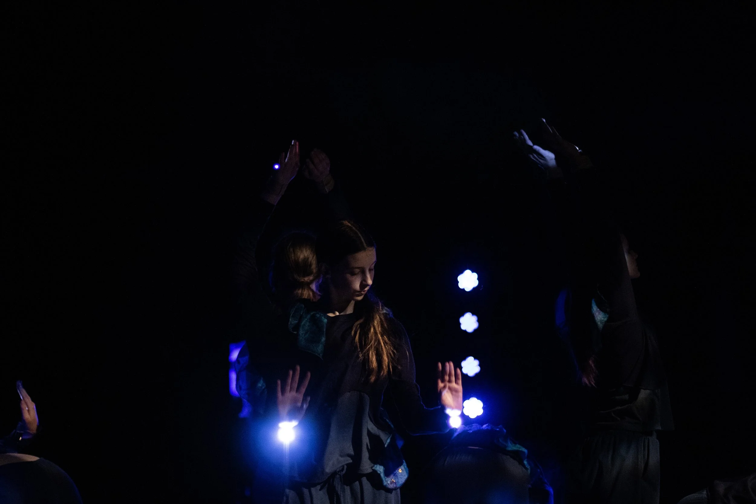 People dancing on a dark stage with blue and purple lighting.