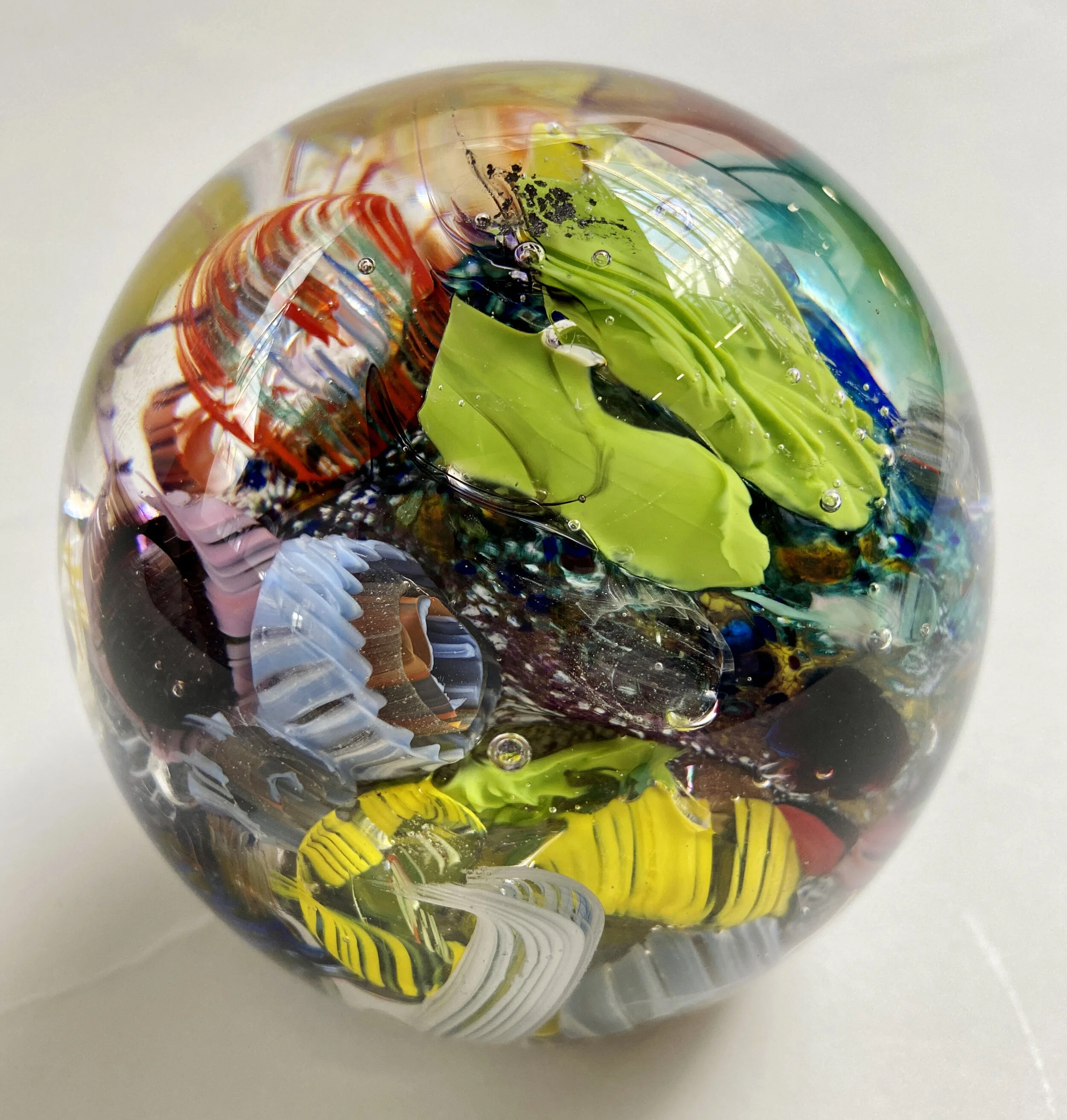 “Ocean Paperweight”
4” Orb
Off Hand Blown Glass 
The largest paperweights of this artist's “Ocean Series". The round shape plays on the multiple layers and 
textures of glass used to create the underwater impression. View from a different side for a 