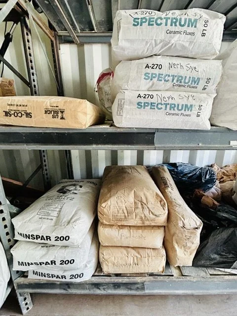 Metal shelving unit with bags of construction materials, including ceramic flux and MinSpar 200, in a storage area