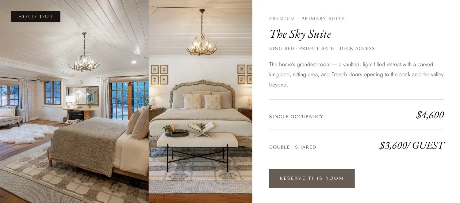 Split view of a hotel room with a bedroom on the right and a living area on the left, featuring light-colored walls, wooden floors, a king bed, and decor with antler chandeliers and framed artwork.