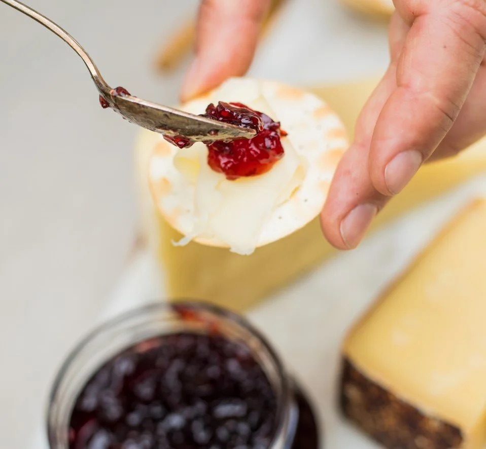 Close-up of someone spreading jam on a slice of soft cheese on a cracker or bread.