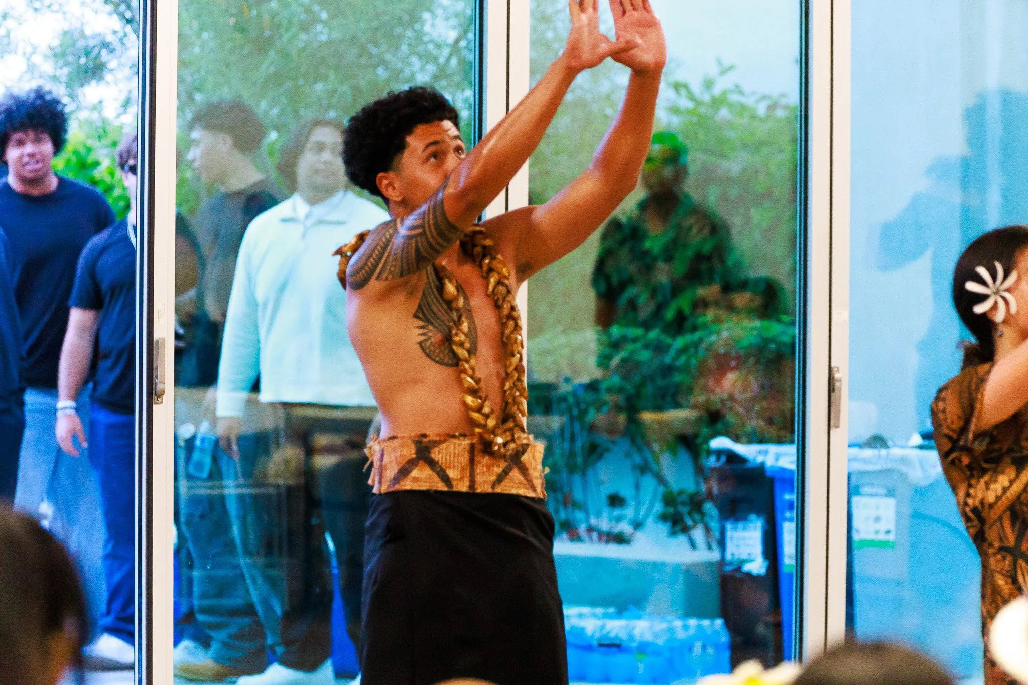 Traditional Polynesian dancer performing with raised arms in front of glass doors
