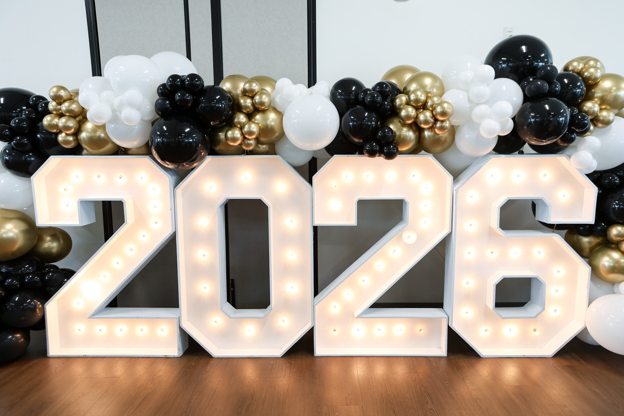 Illuminated white marquee numbers surrounded by black, white, and gold balloons