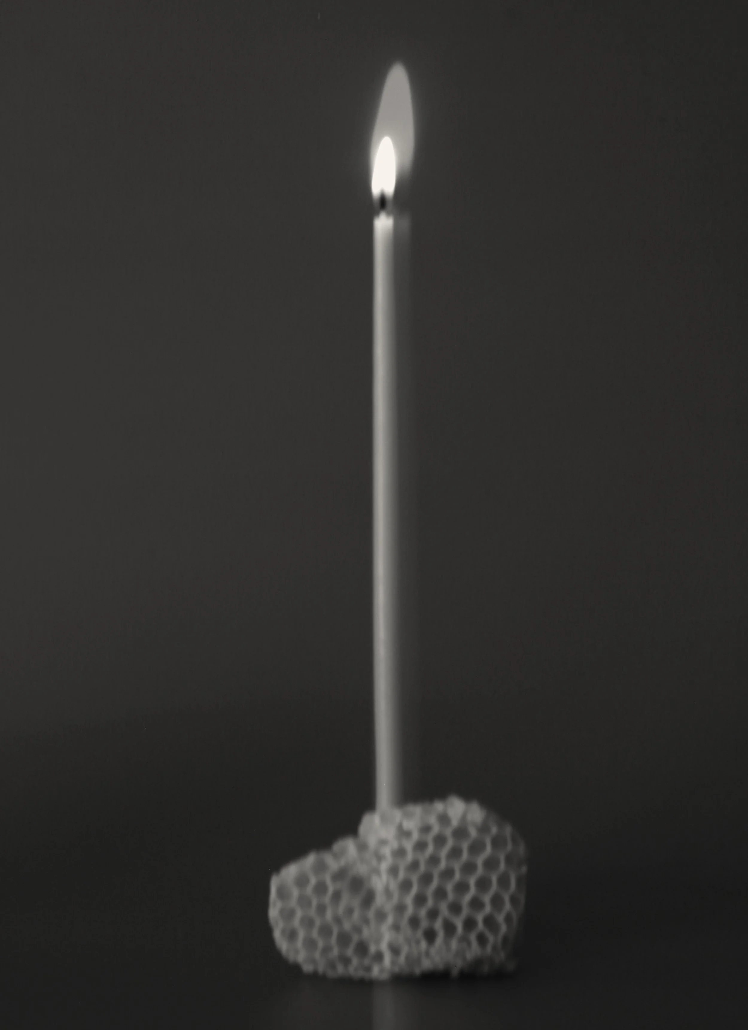 Hand-dipped beeswax taper candle lit against a dark background, photographed as a sculptural ceremonial object.