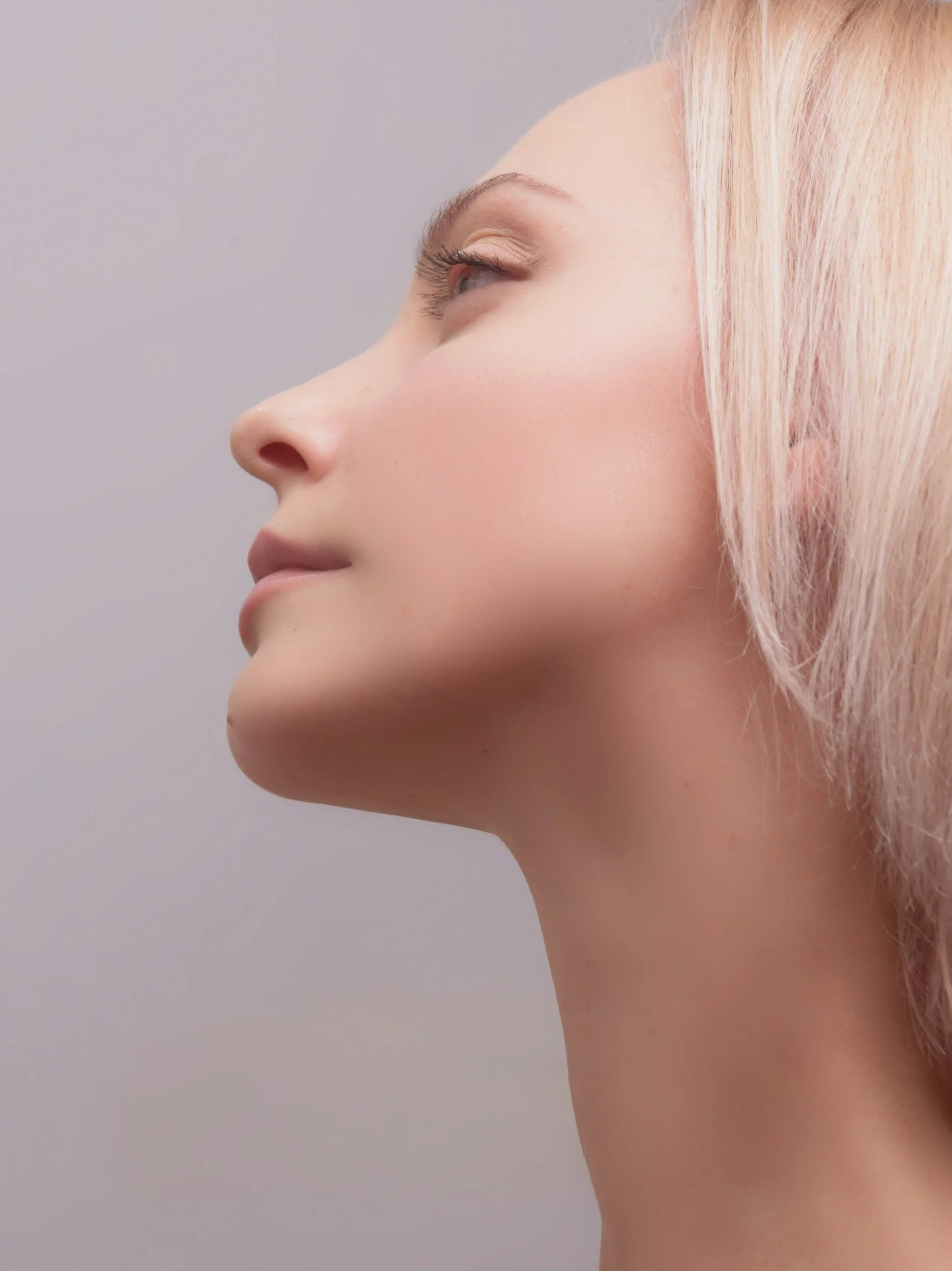Profil d'une femme avec peau claire, cheveux blonds, regardant vers la gauche, fond gris clair. On y voit une mâchoire.