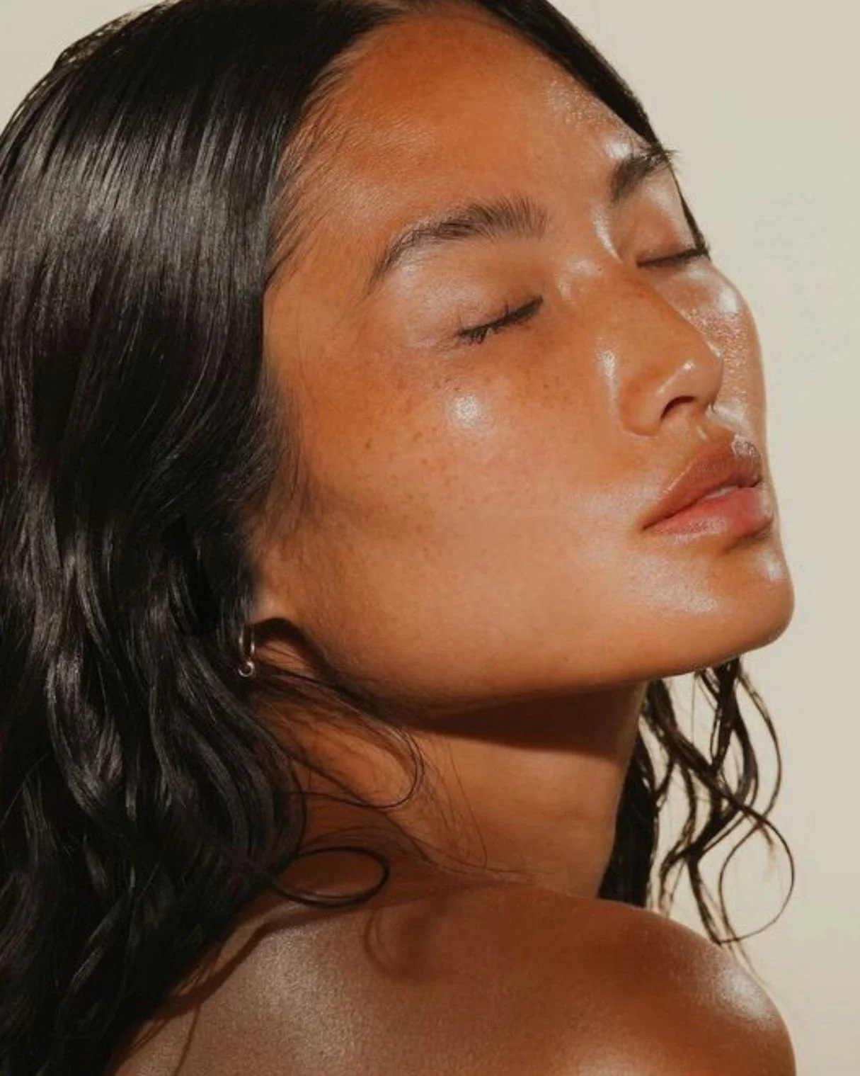 Close-up of a woman with dark wet hair and glowing skin with closed eyes.