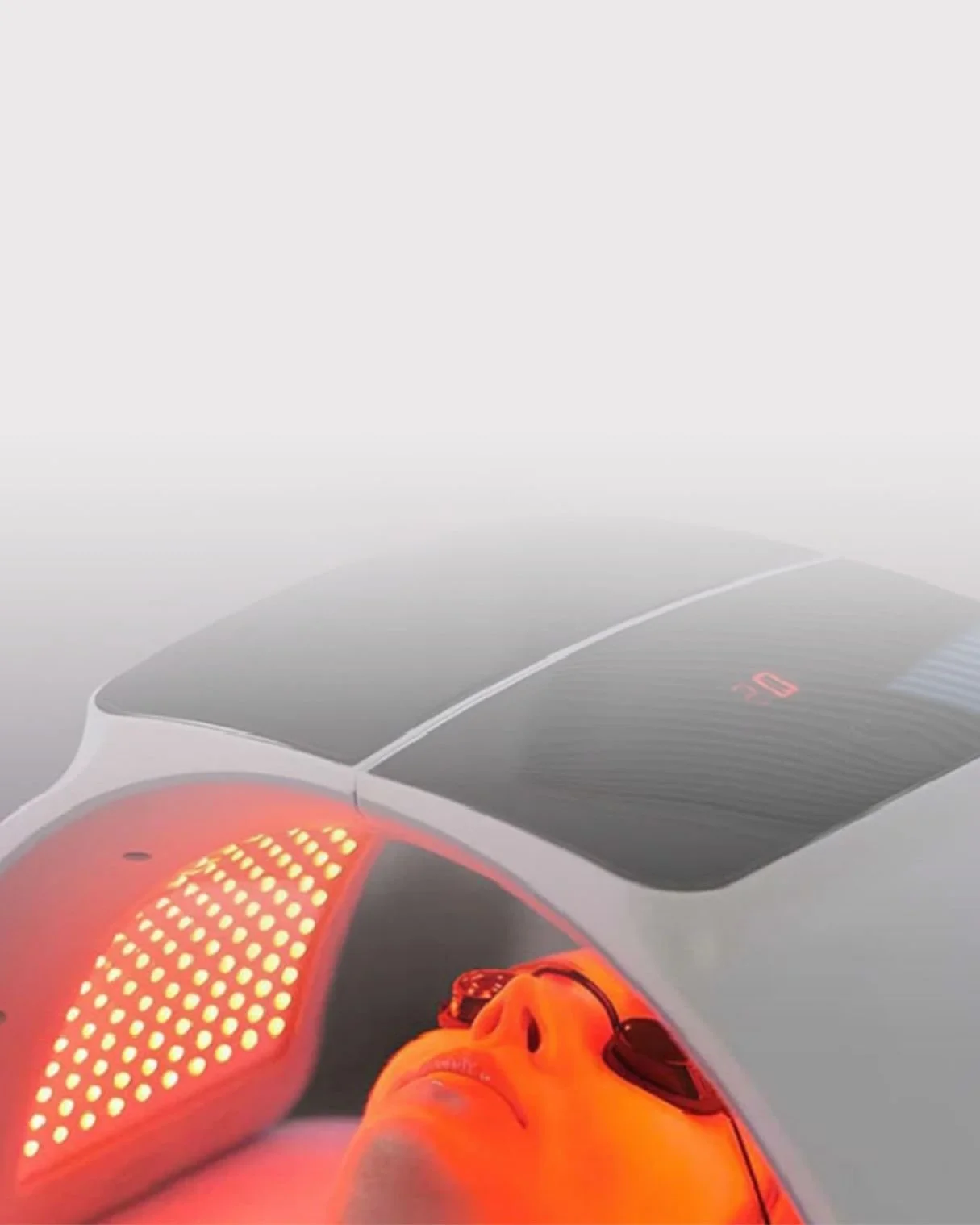 A person lying inside a futuristic red light therapy device with a visor covering their eyes .