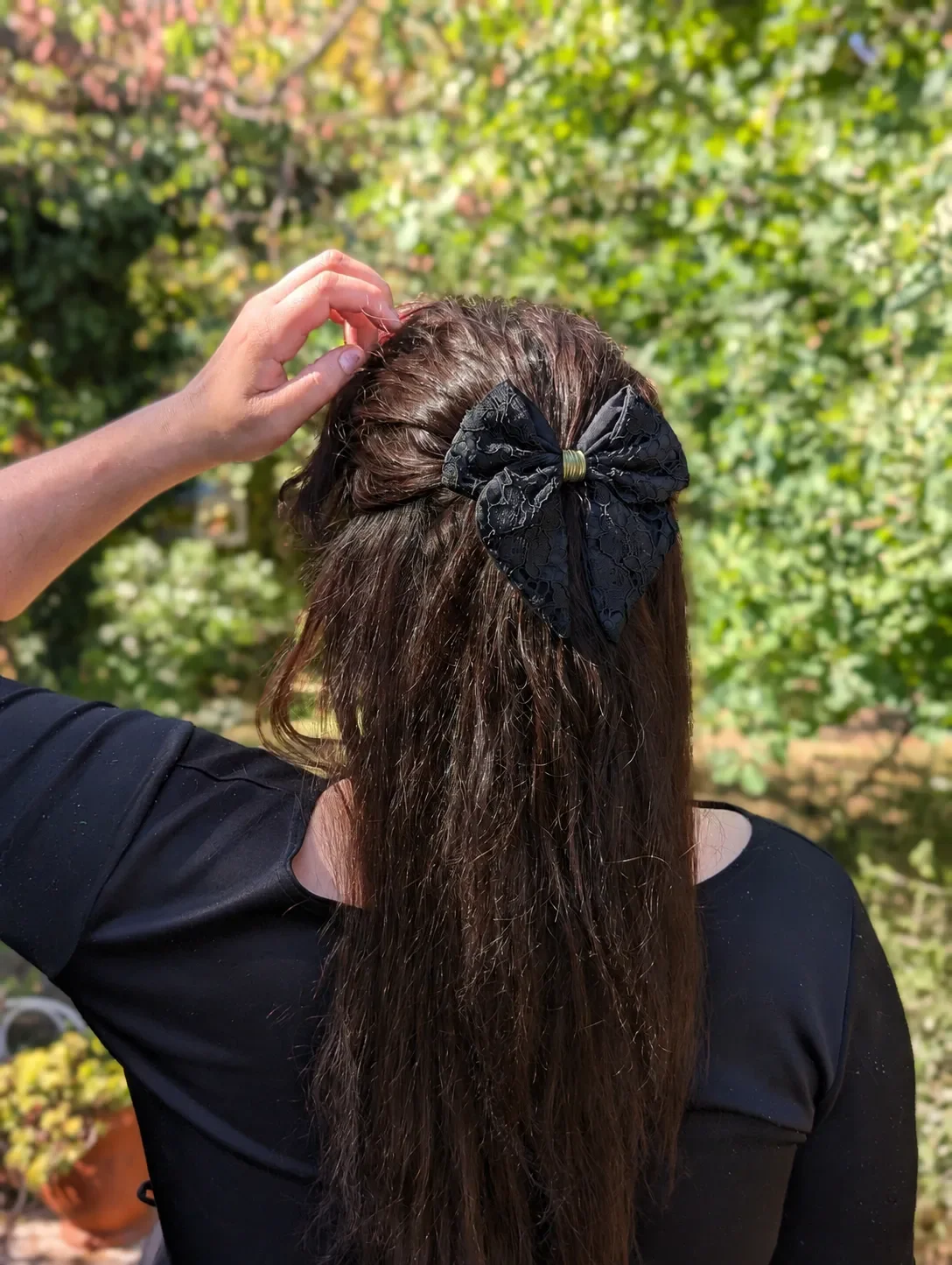 Noeud pour cheveux entièrement noir en dentelle et tissu, porté sur une coiffure semi-attachée.
