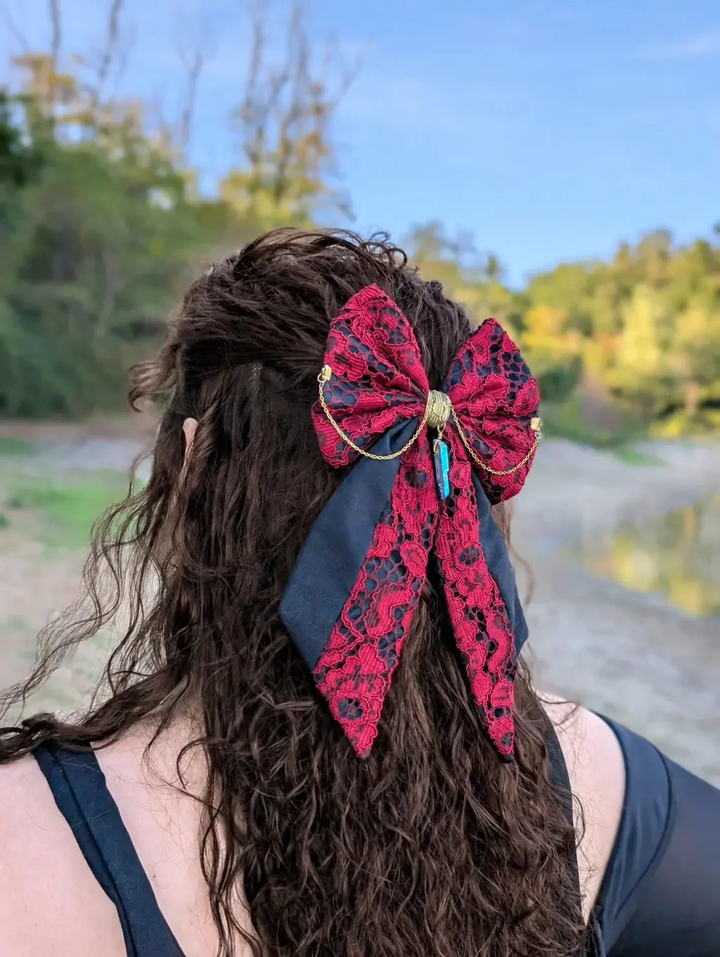 Noeud bijou en dentelle rouge à longues pointes, porté sur cheveux bruns, vue de côté.