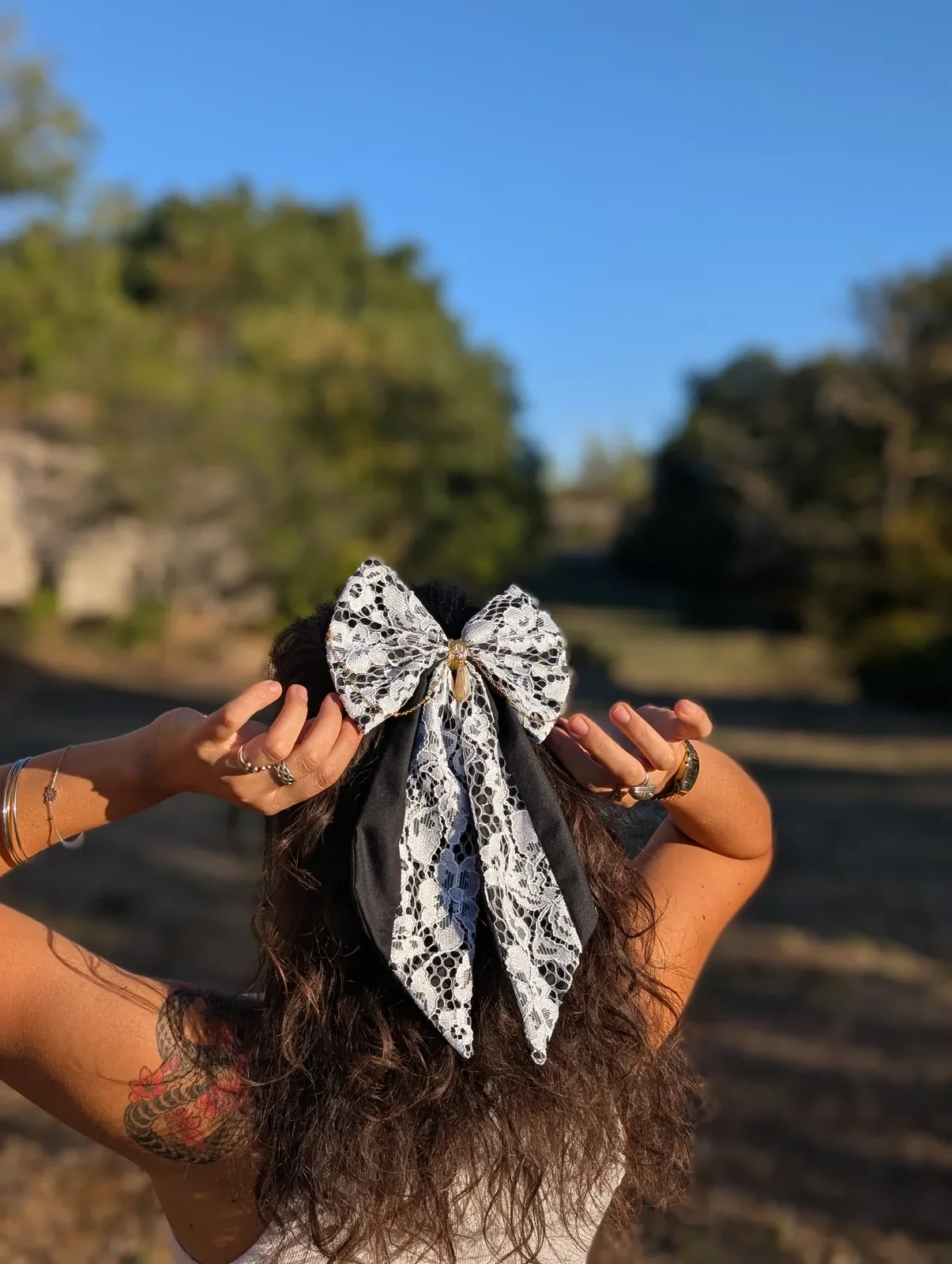 Nœud bijou en dentelle blanche et noire à longues pointes, porté sur cheveux bruns.