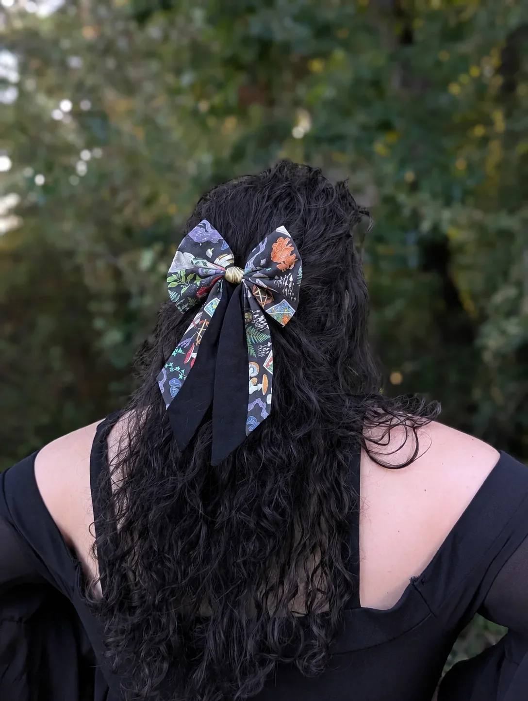 Nœud barrette féerique à longues pointes noires et imprimées, porté sur cheveux bouclés de trois quarts.