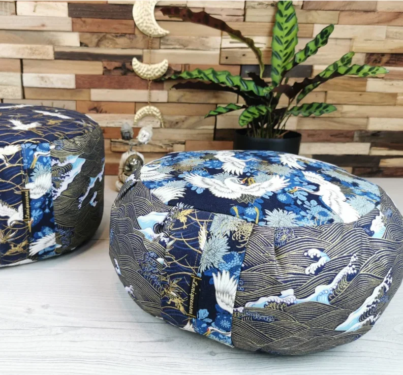 Deux coussins avec des motifs inspirés de l'art japonais traditionnel, posés sur une table en bois, avec un mur en bois derrière et une plante verte en pot.