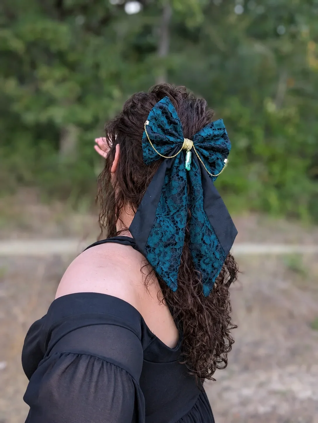 Nœud bijou vert en dentelle à longues pointes, porté sur cheveux bouclés, vue de profil.