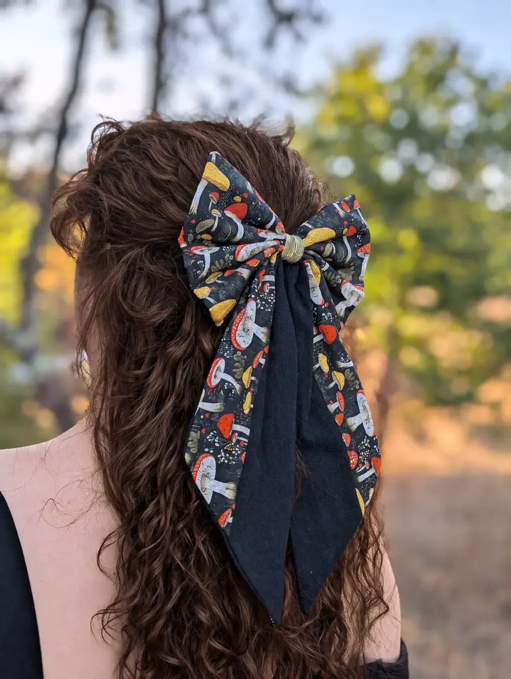Nœud barrette Mycélia à champignons rouges et jaunes avec longues pointes noires sur cheveux bruns.