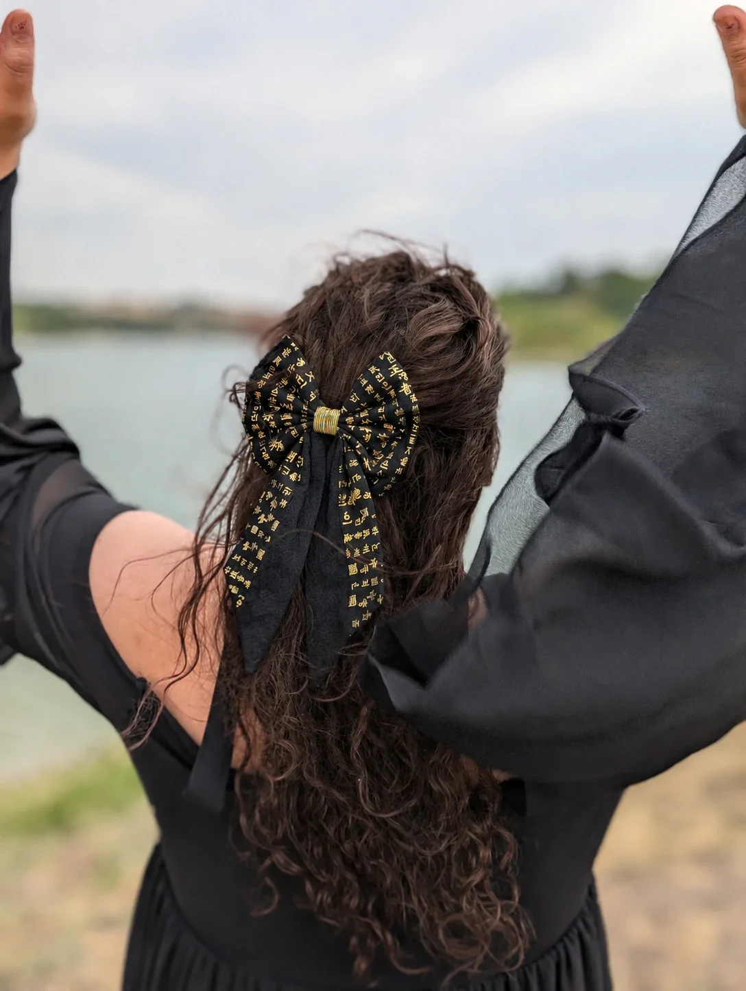 Grand nœud barrette Hangeul noir et or porté sur une coiffure semi-attachée, vue de dos, au bord d'un lac.