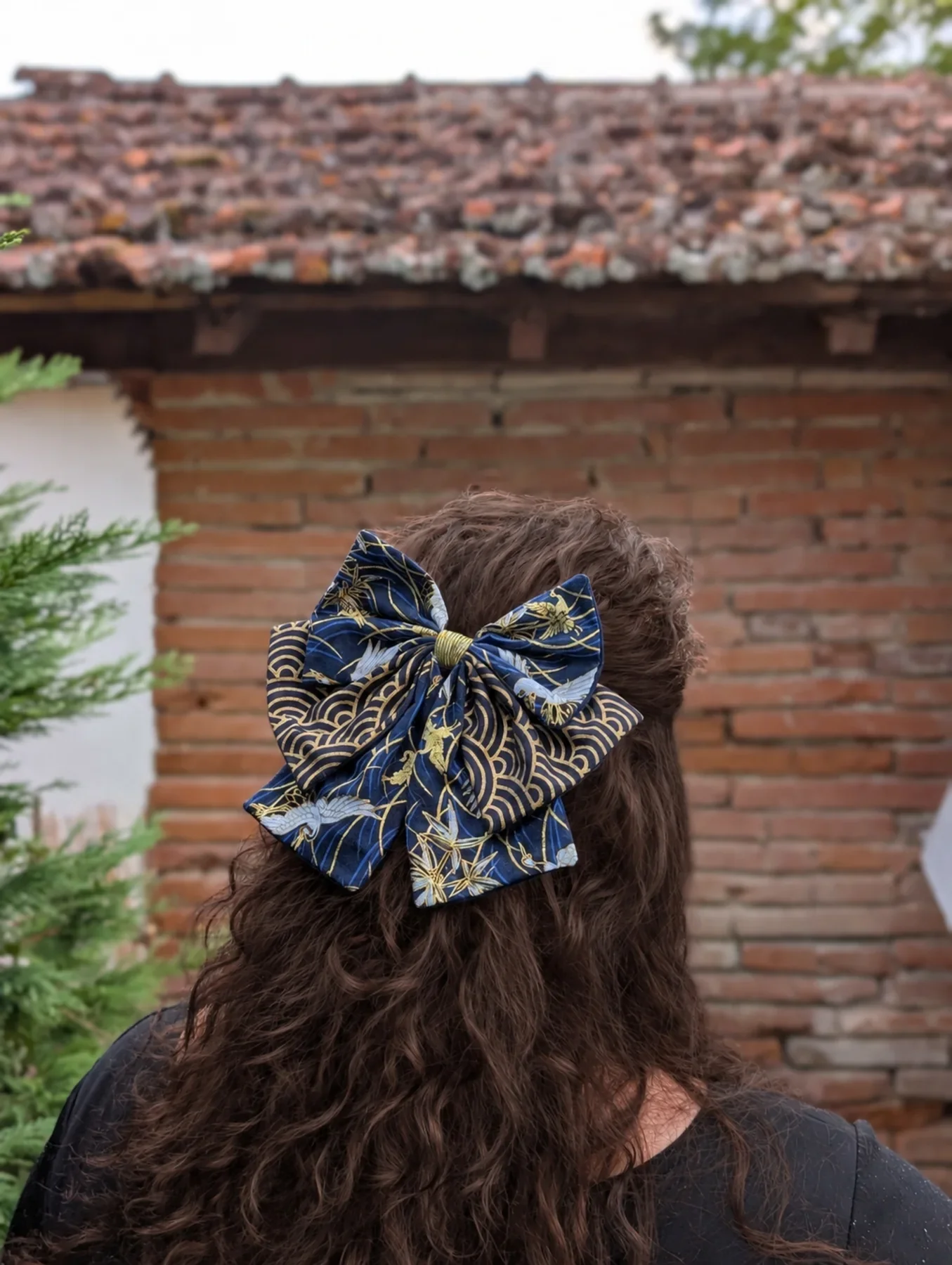 Noeud japonais Tsuru bleu nuit a grues et vagues dorees sur cheveux bruns boucles.