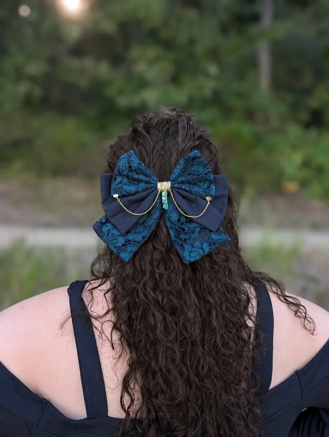 Noeud bijou vert en dentelle et chaînes dorées sur cheveux bruns bouclés, vu de dos.