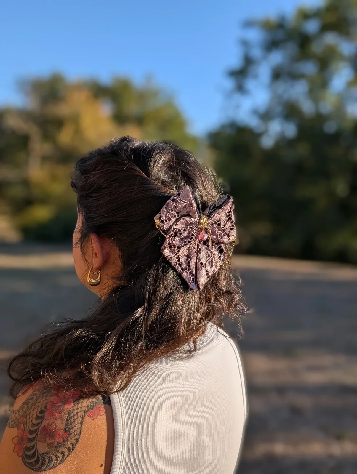 Nœud bijou rose poudré et noir en dentelle, chaînes dorées et cristal rose, vue de côté.