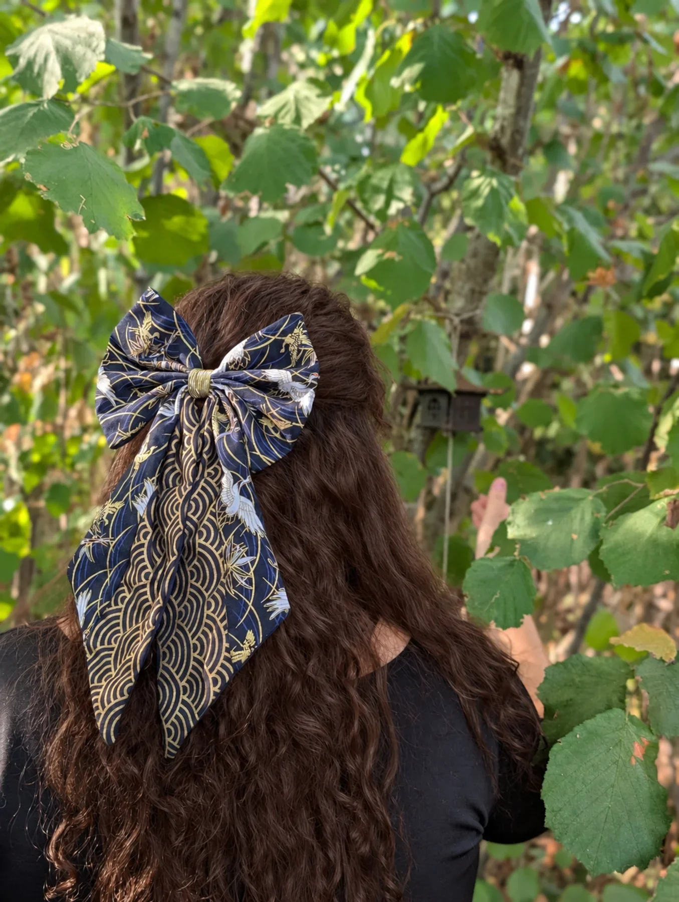 Grand noeud Tsuru bleu nuit a longs pans et vagues dorees sur cheveux bruns boucles.