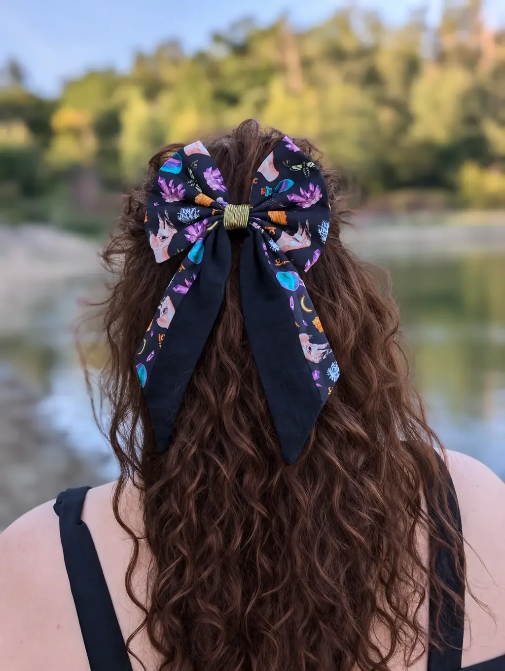 Nœud Clés d’Arcane à motifs de cristaux et fioles avec pans noirs porté sur cheveux bruns bouclés.