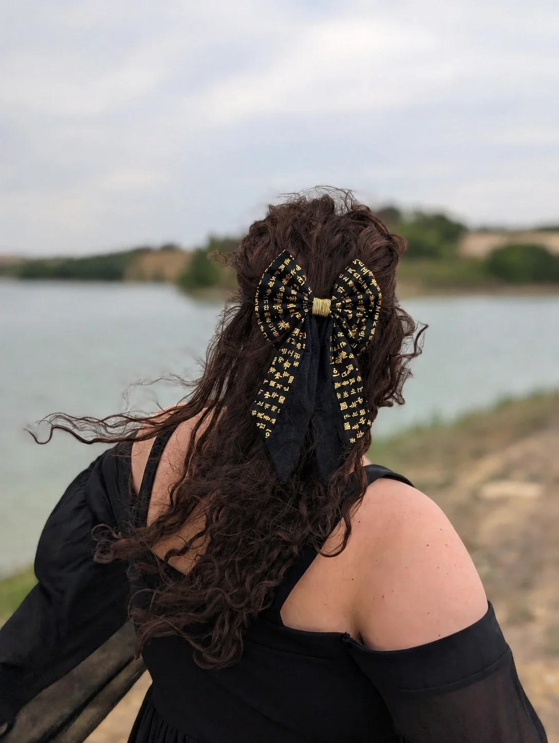 Nœud pour cheveux Hangeul noir à écritures dorées, porté sur cheveux longs bouclés en extérieur.