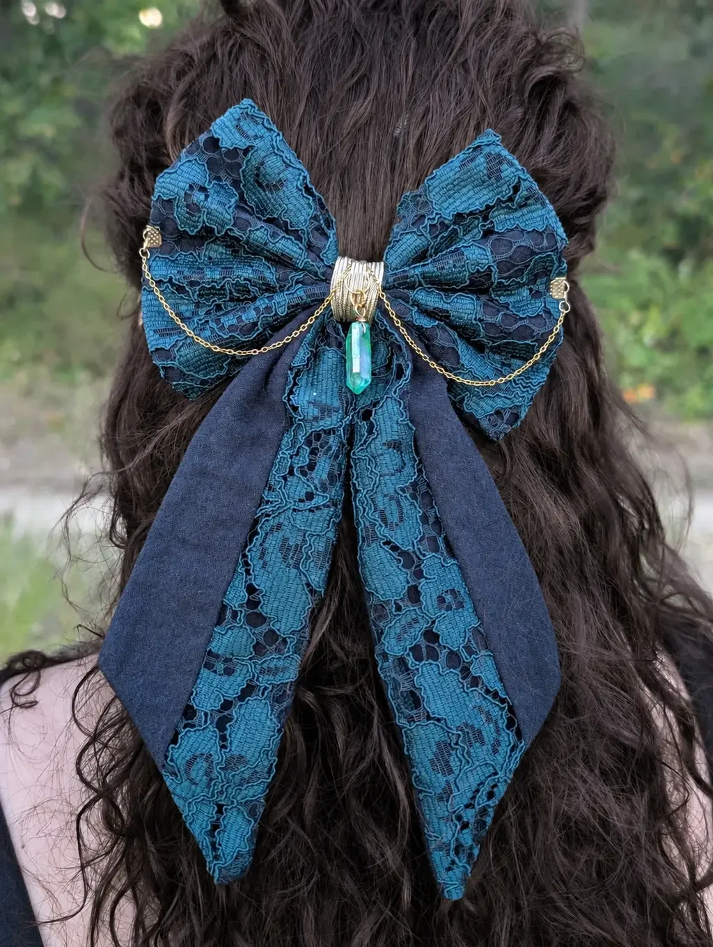 Noeud bijou en dentelle verte à longues pointes, porté sur cheveux bruns, vue rapprochée.